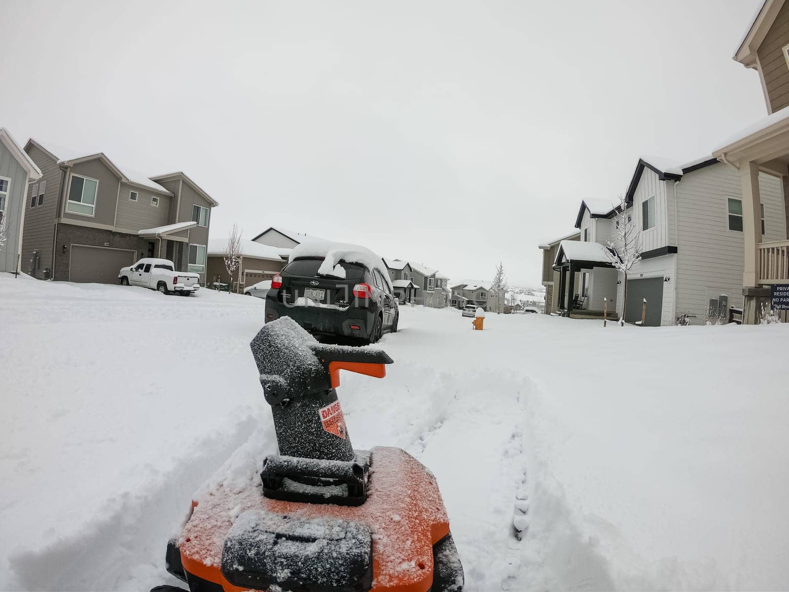 Denver, Colorado, USA-February 4, 2024-View from a snow-blanketed driveway captures a residential area mid-snowfall, with houses partially obscured by the cascading white flakes and a snow-covered car in the foreground.