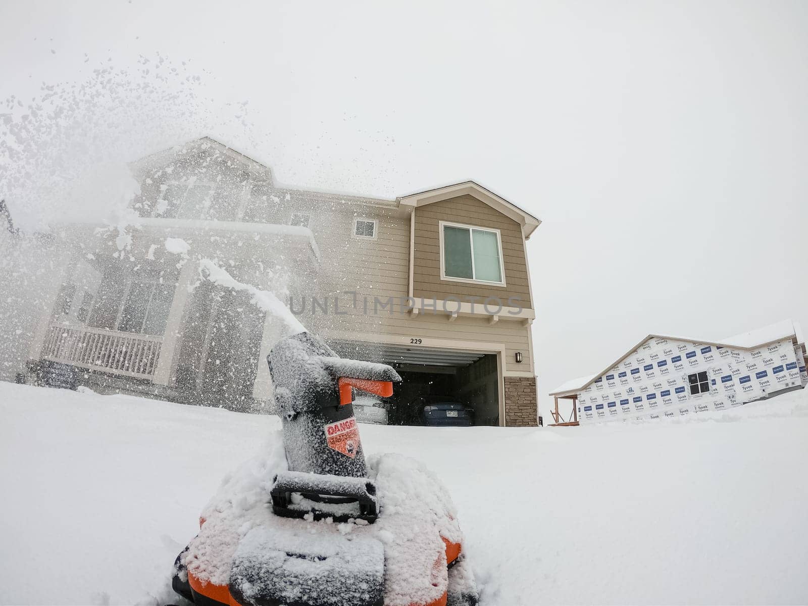 Denver, Colorado, USA-February 4, 2024-View from a snow-blanketed driveway captures a residential area mid-snowfall, with houses partially obscured by the cascading white flakes and a snow-covered car in the foreground.
