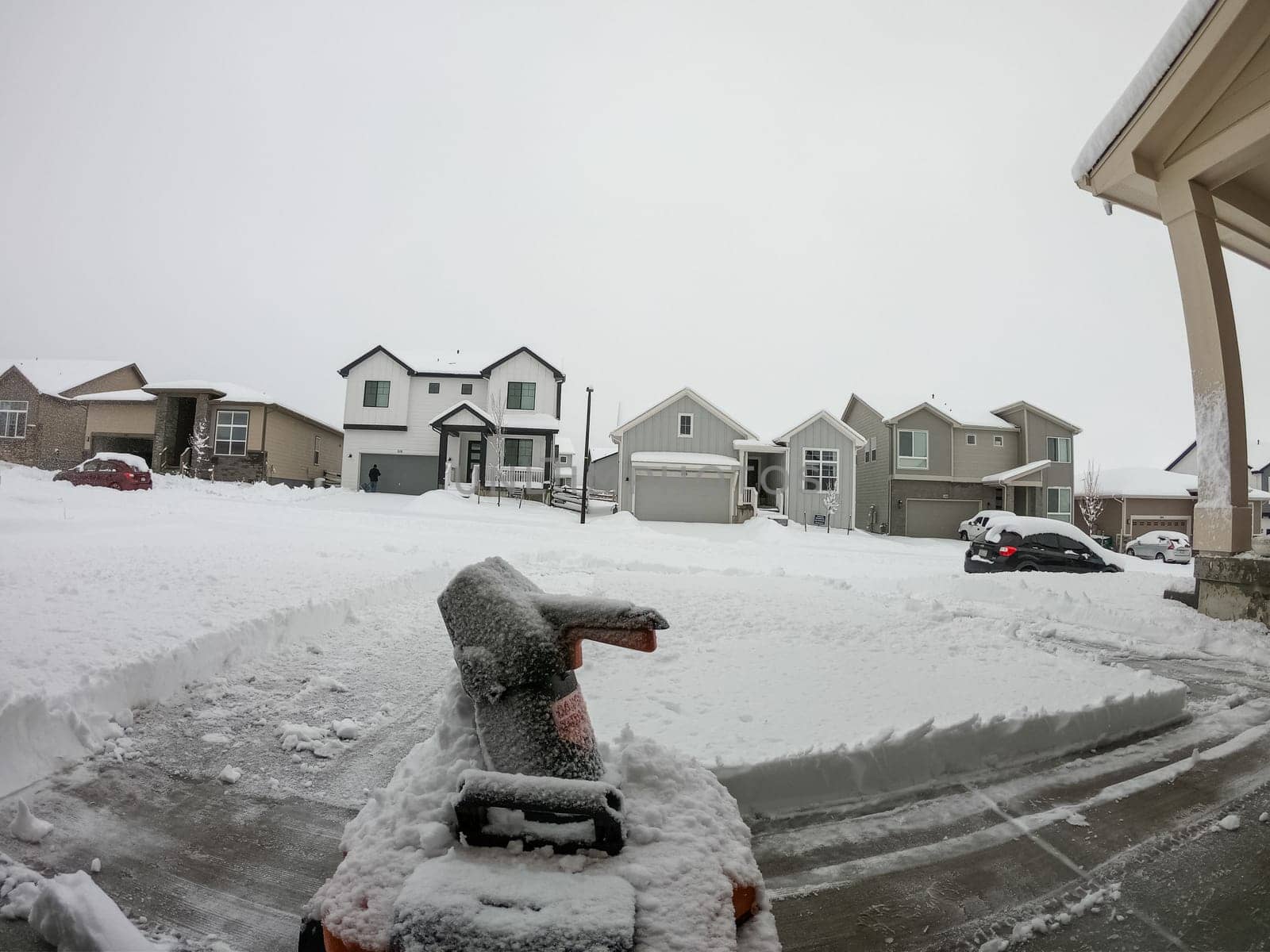 Denver, Colorado, USA-February 4, 2024-View from a snow-blanketed driveway captures a residential area mid-snowfall, with houses partially obscured by the cascading white flakes and a snow-covered car in the foreground.