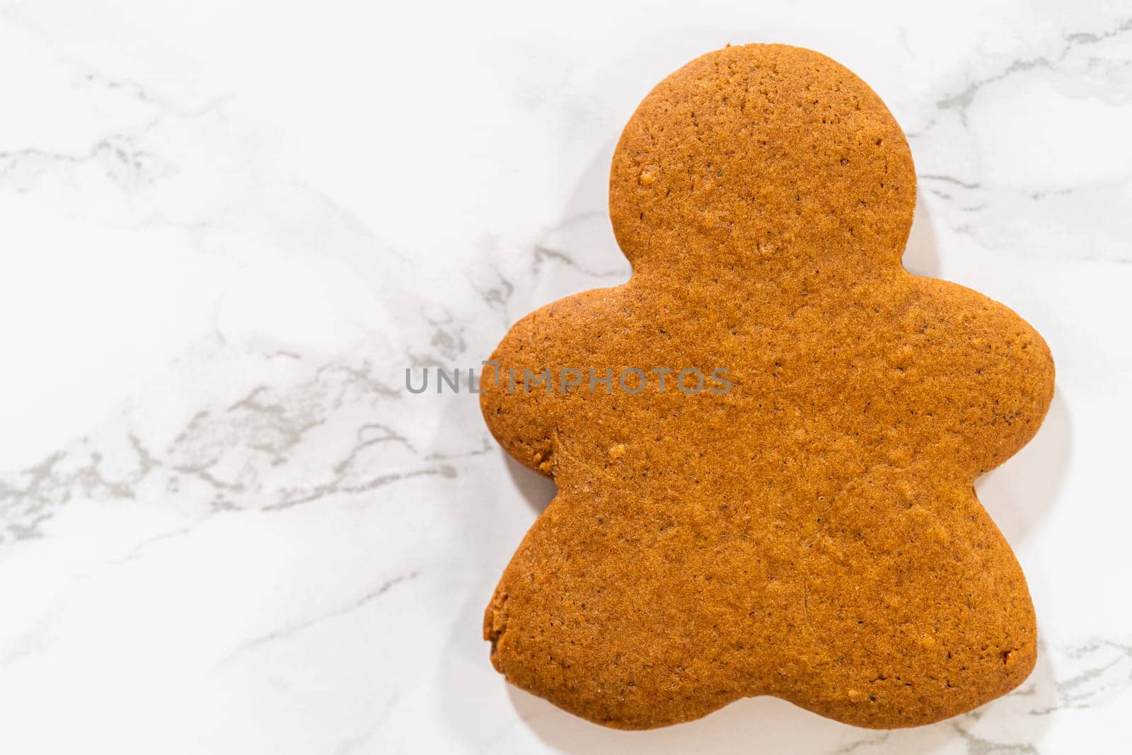 A single Orange Zest Gingerbread Cookie in gingerbread girl shape placed on a white marble background, highlighting its rich color and smooth finish.