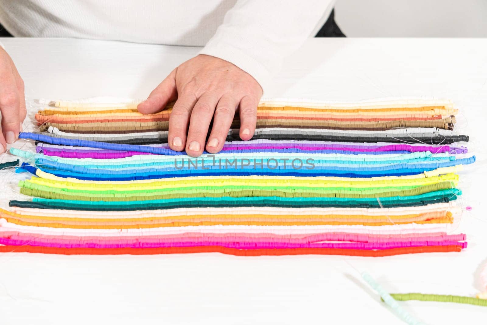 A vibrant collection of clay beads, neatly arranged by color on a white table, ready to inspire young crafters to create their own unique bracelets.