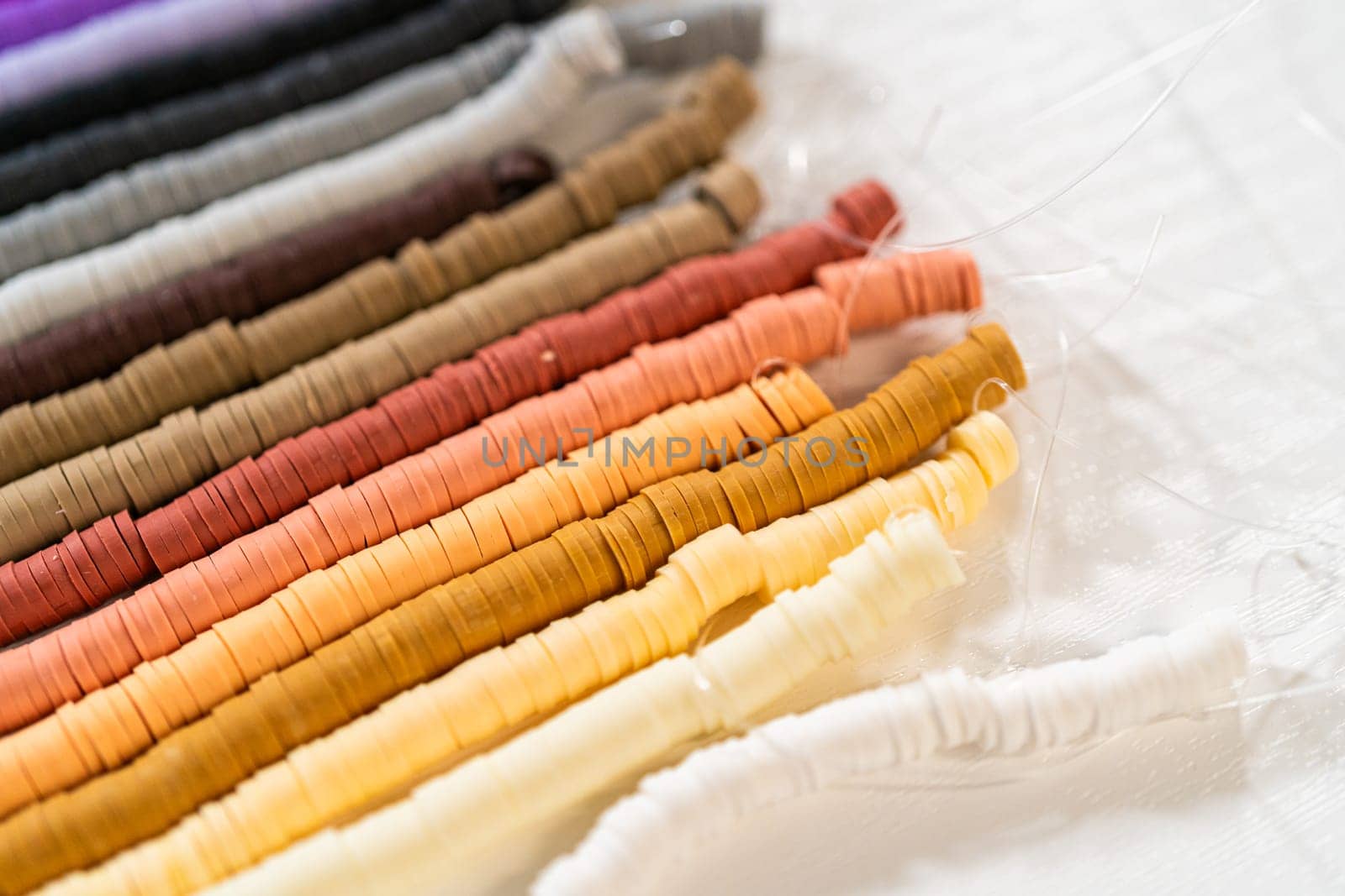 A vibrant collection of clay beads, neatly arranged by color on a white table, ready to inspire young crafters to create their own unique bracelets.