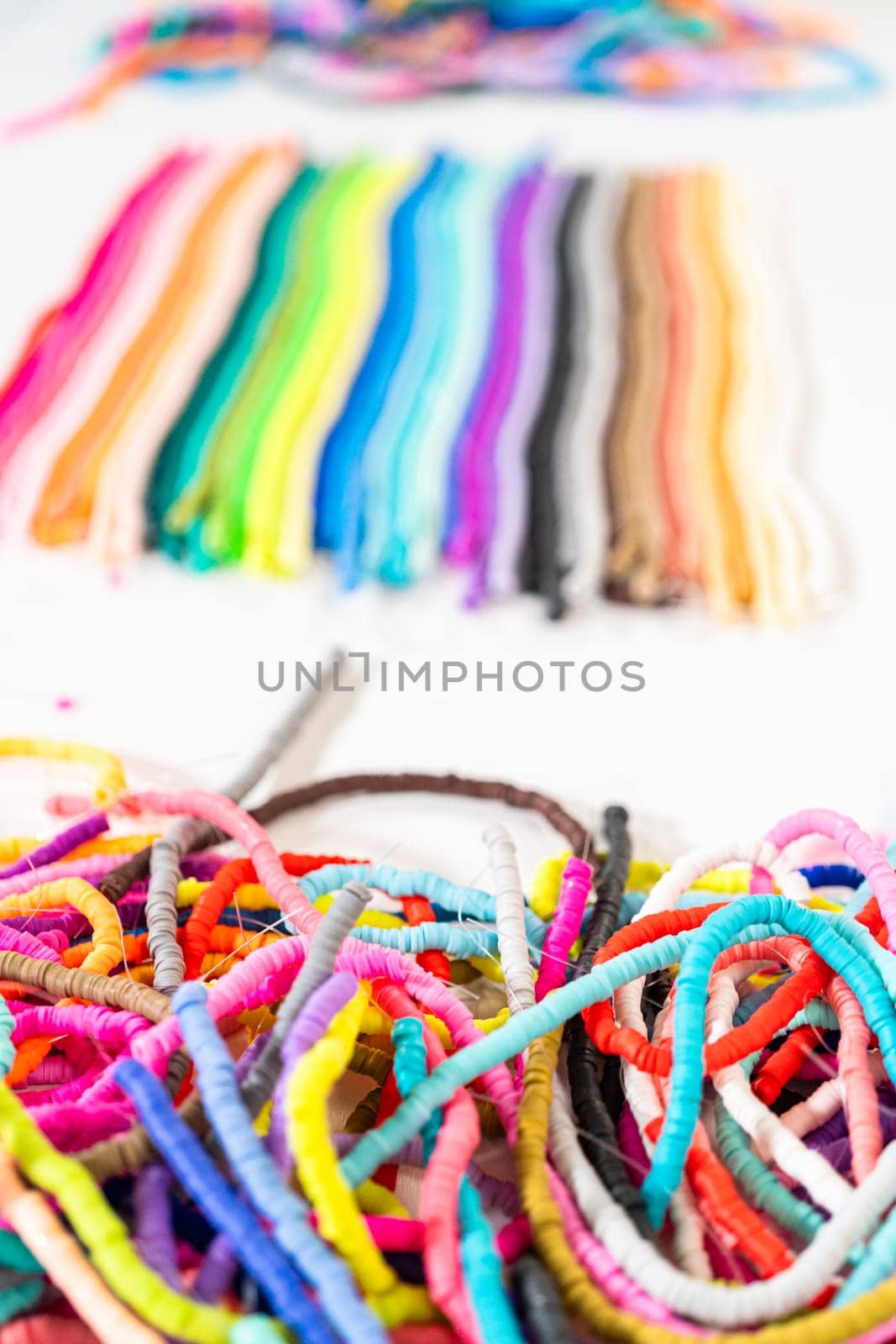 A vibrant collection of clay beads, neatly arranged by color on a white table, ready to inspire young crafters to create their own unique bracelets.