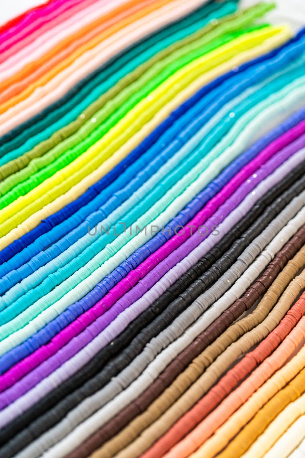 A vibrant collection of clay beads, neatly arranged by color on a white table, ready to inspire young crafters to create their own unique bracelets.