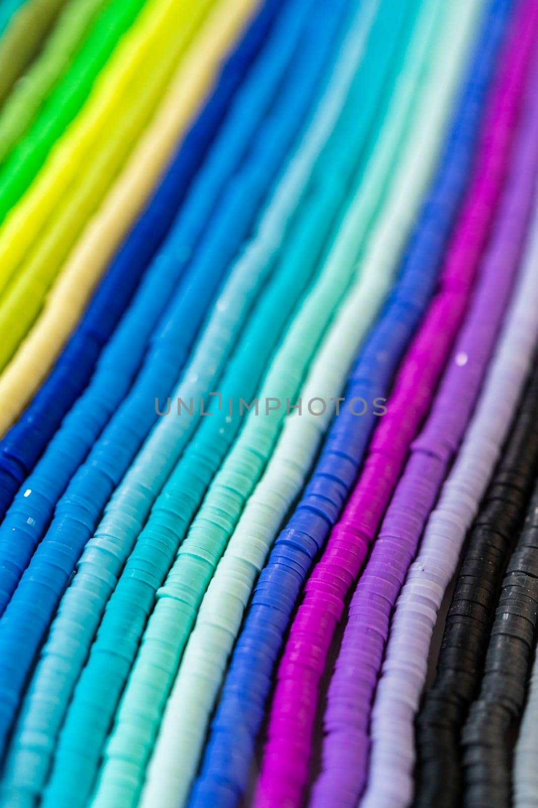 A vibrant collection of clay beads, neatly arranged by color on a white table, ready to inspire young crafters to create their own unique bracelets.