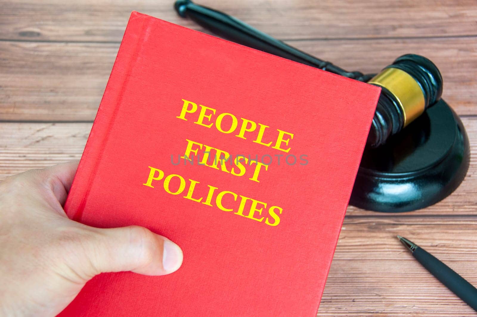 Hand holding People First Policies book with gavel on a wooden table background.