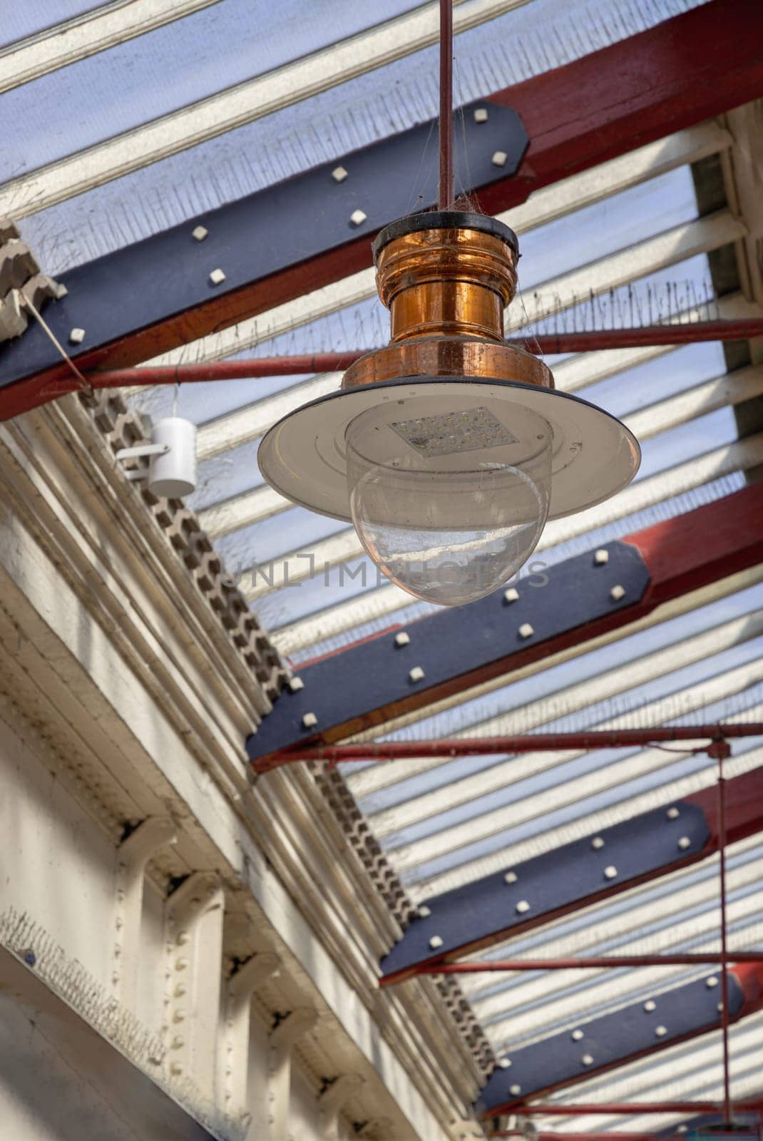 Windsor, England - Apr 3, 2025 - A vintage copper ceiling light fixture with a glass globe shade hangs from a white ceiling and Wooden beams are visible creating a rustic yet elegant interior atmosphere at Windsor & Eton Riverside railway station. Paddington pendant light, use it as your Wallpaper, Poster and Copy space, Selective focus.