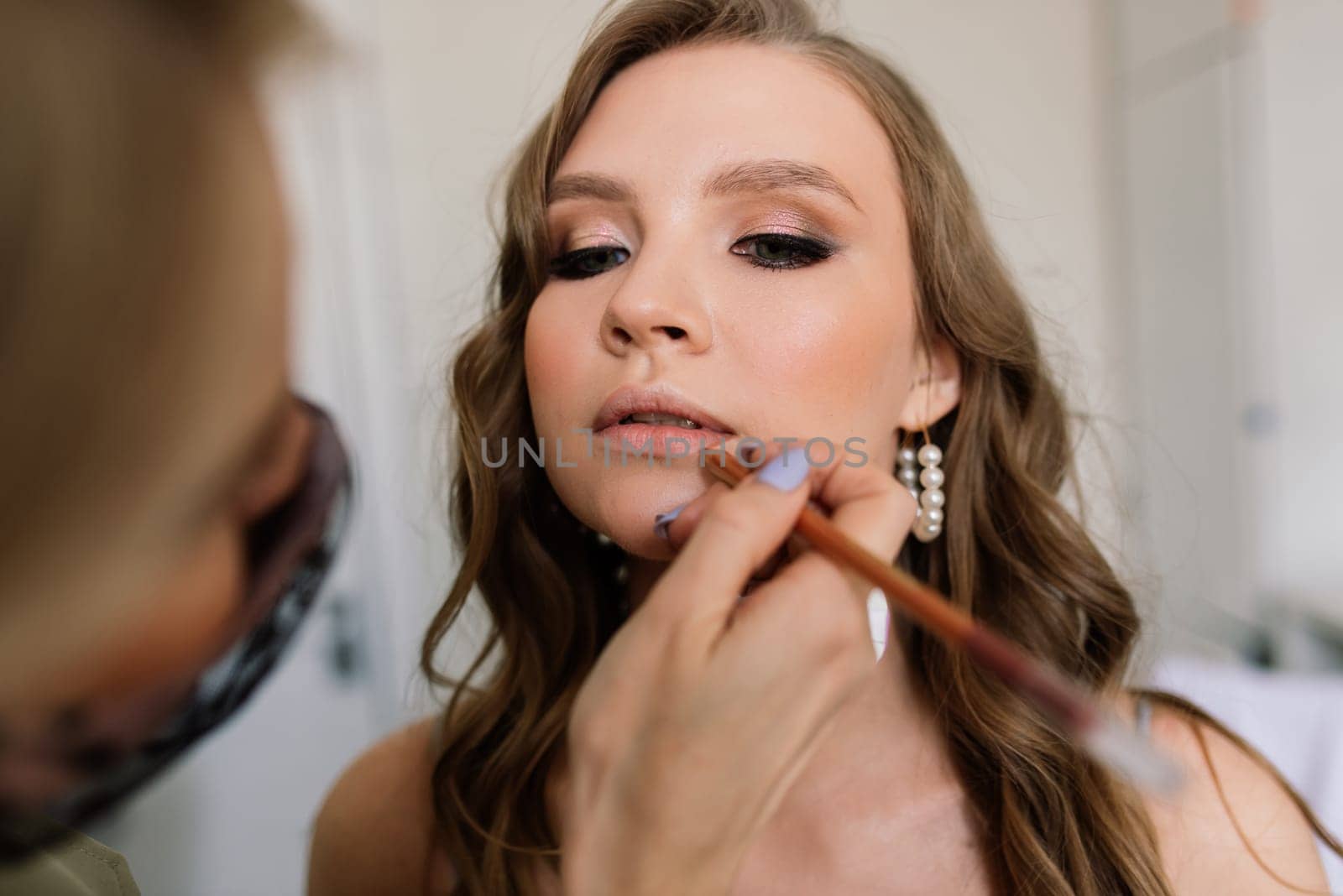 Makeup artist applies lipstick. Hand of make-up master, painting lips of a young beauty model.