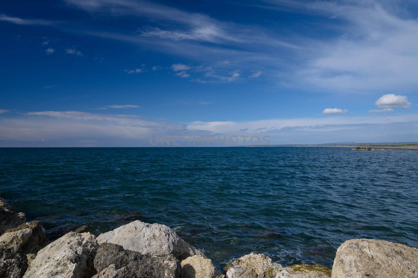 A serene coastline stretches out, with clear blue waters mingling with rocky formations. Wispy clouds drift lazily across the sky, creating a picturesque scene of nature's beauty.