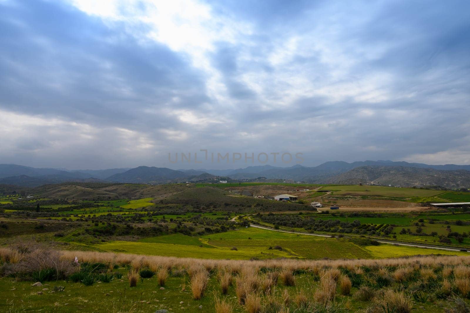 Beneath a blanket of swirling clouds, lush green hills stretch across the horizon, inviting exploration in a tranquil countryside setting. Nature thrives in this serene vista.