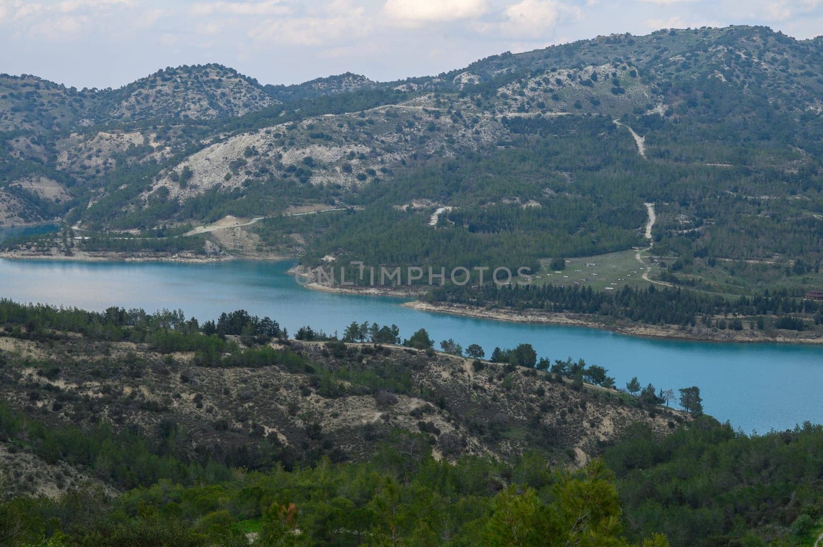 Majestic mountains cradle a sparkling blue lake, reflecting the sky above. A tapestry of green trees stretches along the shore, inviting tranquility and exploration in nature's embrace.