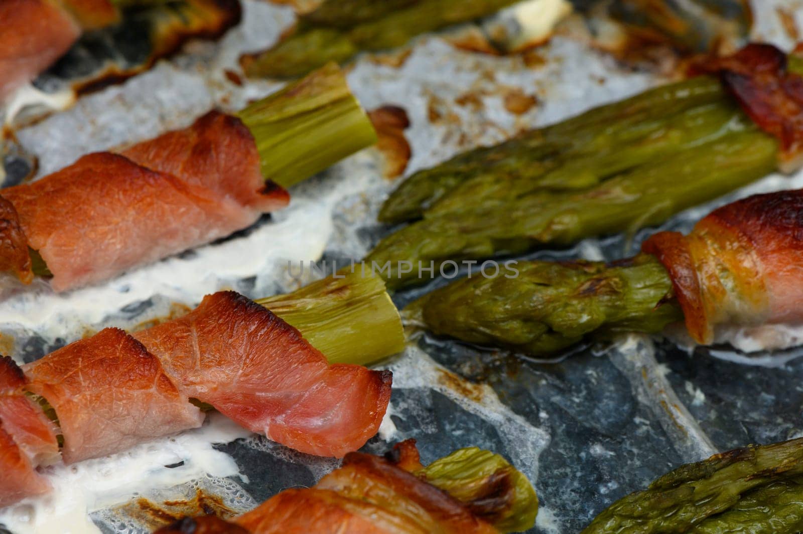 Asparagus spears are nestled in crispy bacon, sizzling under the radiant warmth of the oven. The colors of green and brown blend harmoniously, evoking a delightful culinary experience.