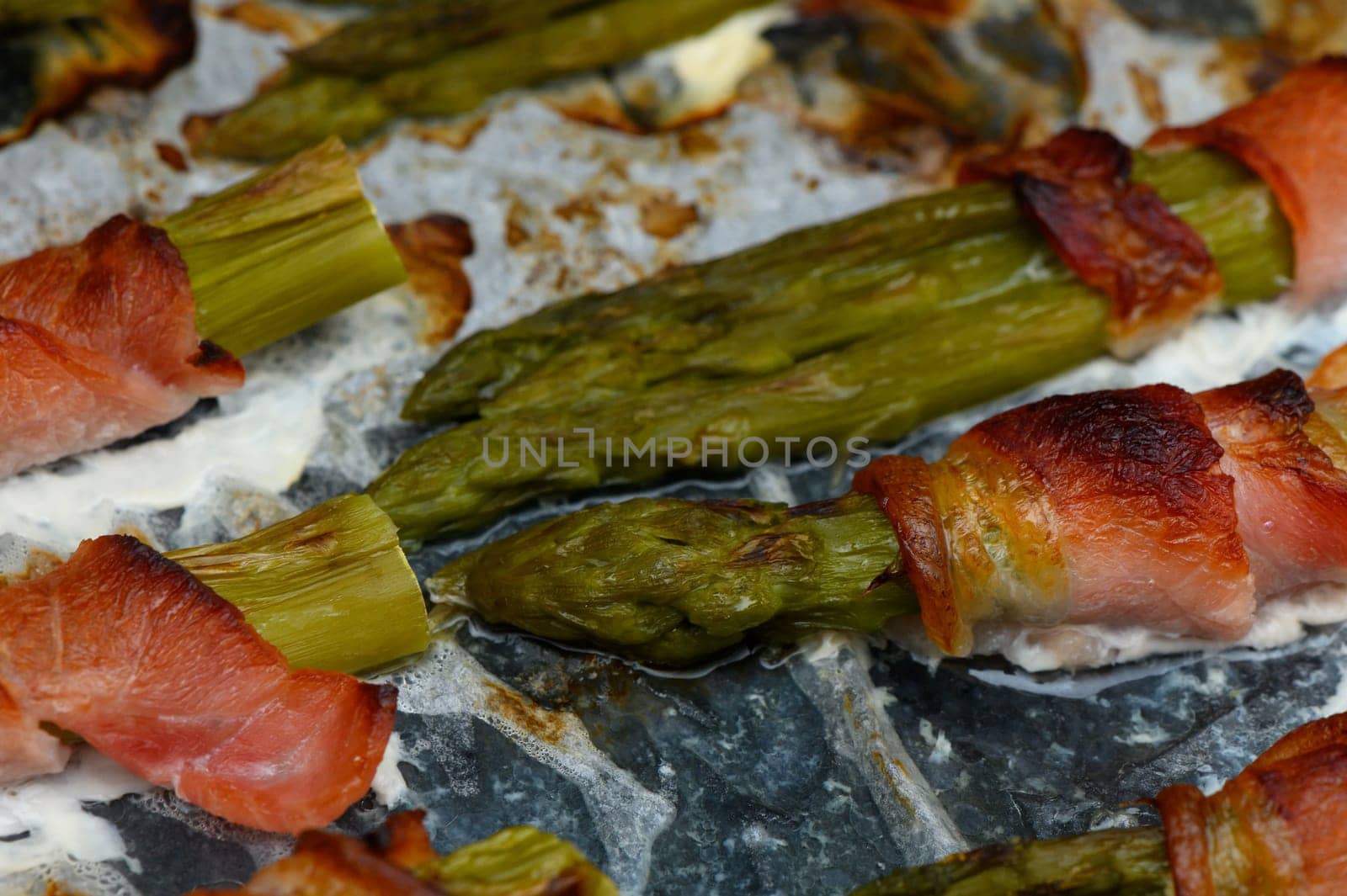 Succulent asparagus spears are artfully wrapped in crispy bacon, sizzling on a grill during an inviting sunset gathering. The aroma fills the air, creating a warm atmosphere for sharing.