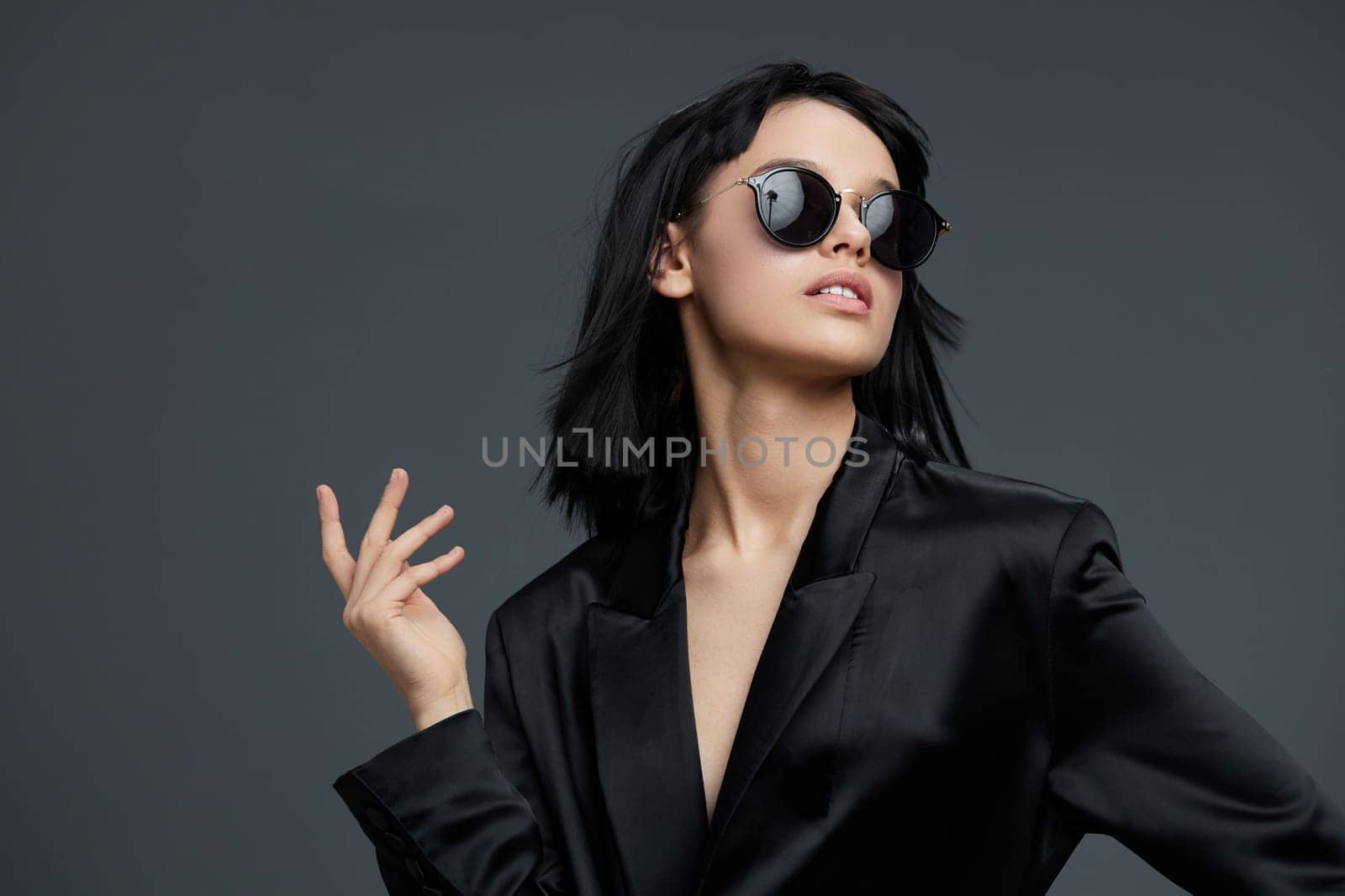 Woman, black suit, sunglasses a confident woman in a sleek black suit and stylish sunglasses poses for the camera with one hand on her hip while placing a finger on her lips, exuding sophistication