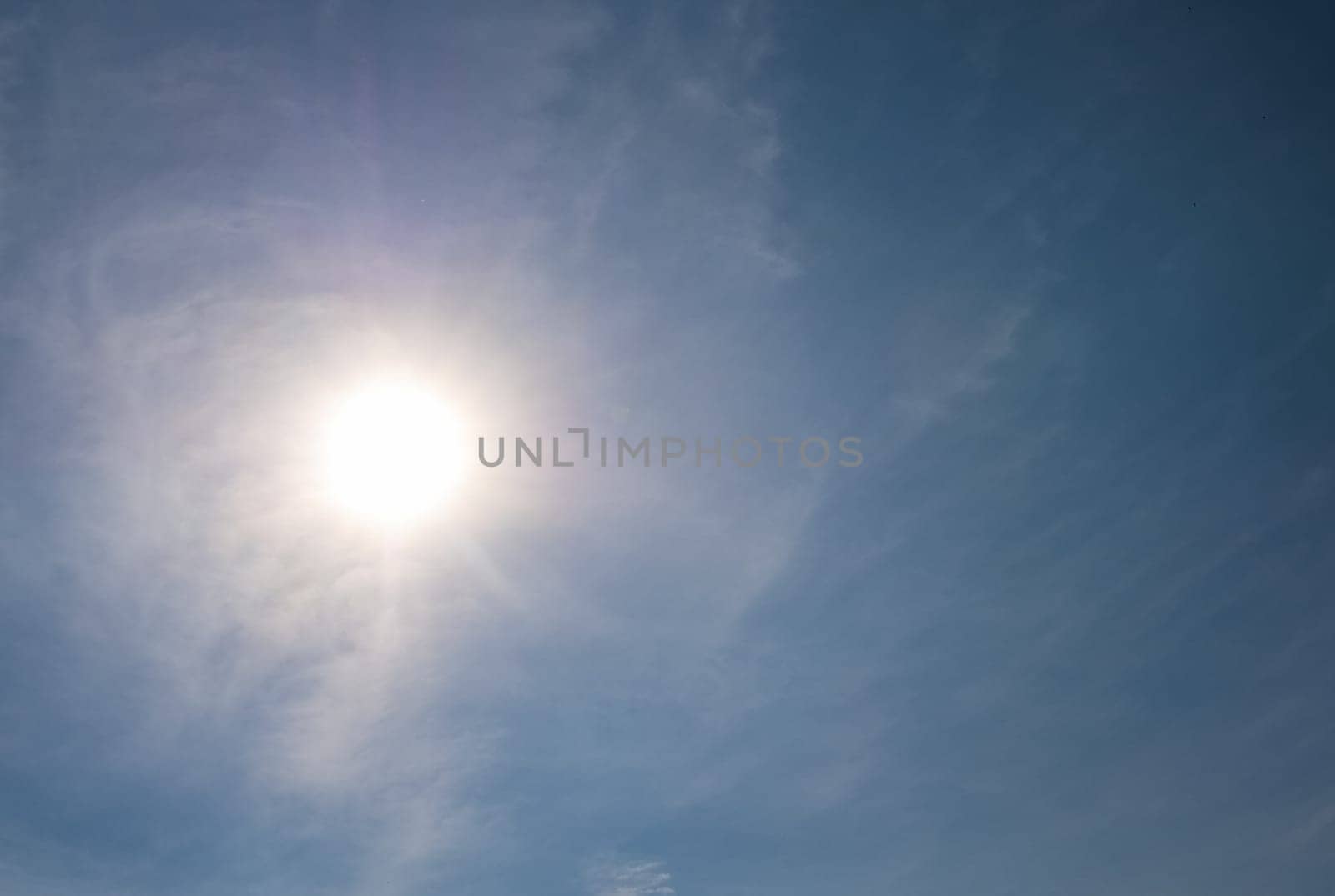 Sun shining through wispy clouds in a clear blue sky, creating a beautiful natural background