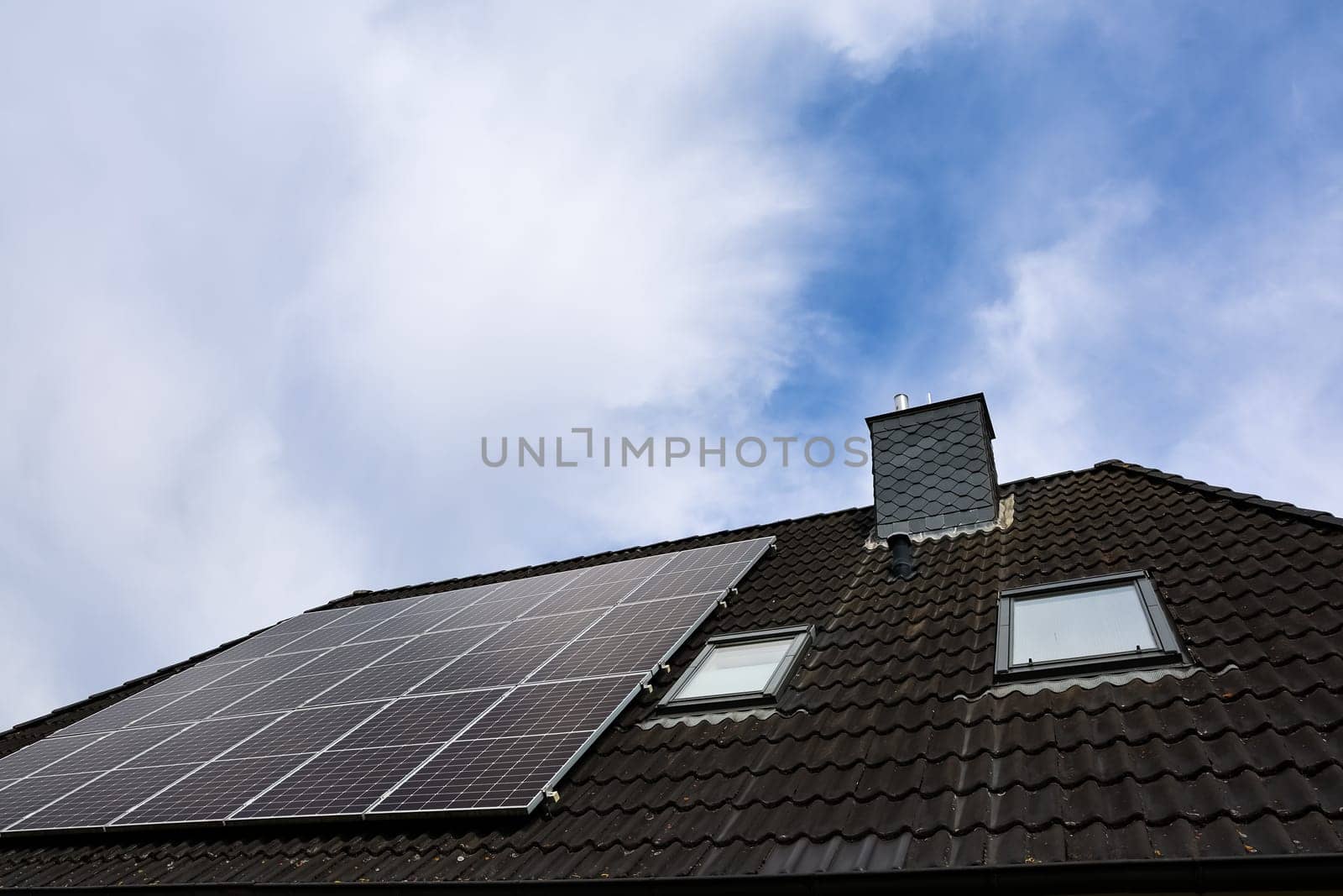 Photovoltaic panels installed on a rooftop with chimney and skylights, providing clean energy under a cloudy sky