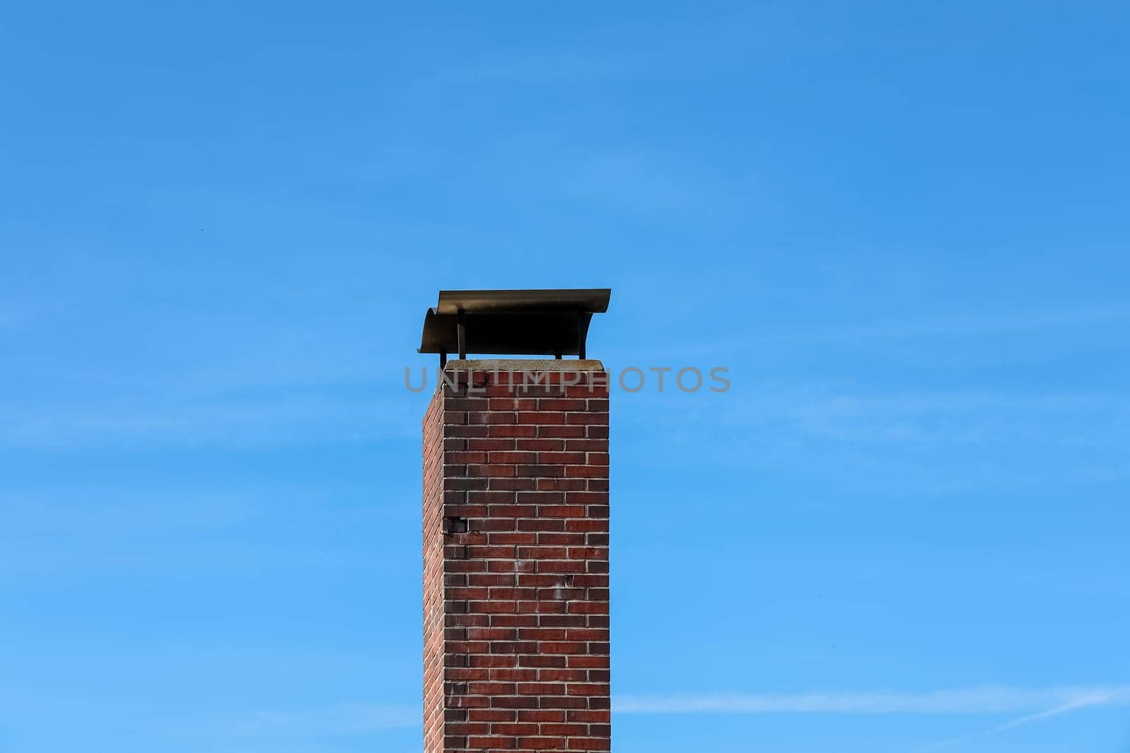 Red brick chimney rising tall with a sleek metallic chimney cowl, set against a backdrop of a vibrant clear blue sky