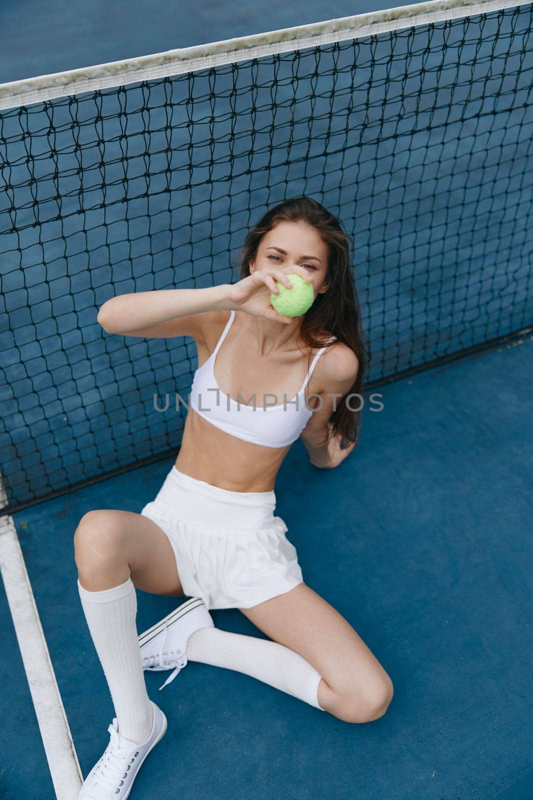 A healthy and happy young woman on a tennis court, savoring a green apple She is dressed in a white athletic outfit, showcasing a vibrant lifestyle and sporty energy
