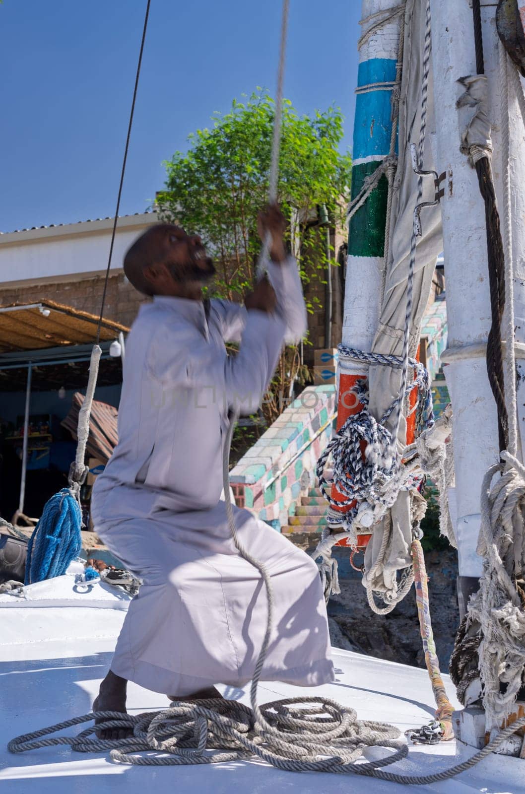 Sailor in traditional Egyptian clothing raising the sail on a felucca sailboat prior to river Nile cruise