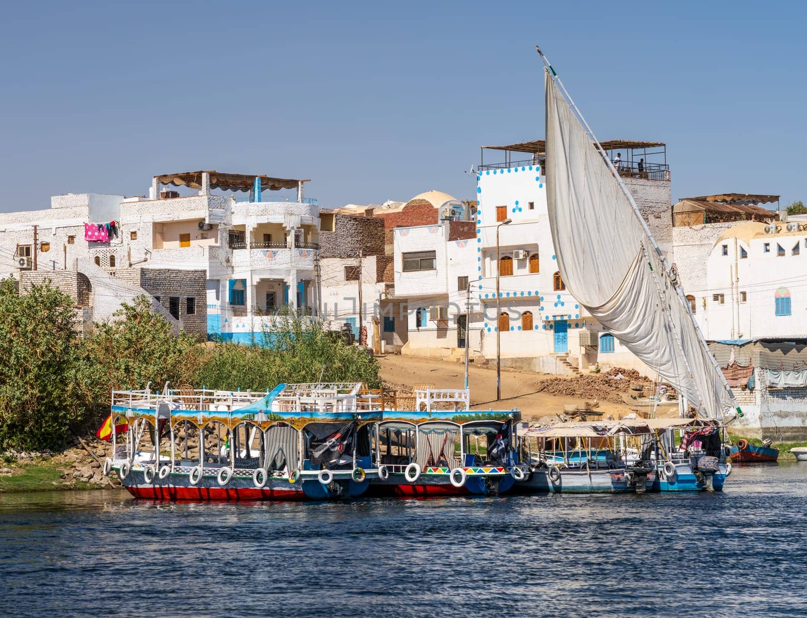 Homes line the shores of Nile on Elephantine island with ferry boats and cruise boats docked alongside in Aswan