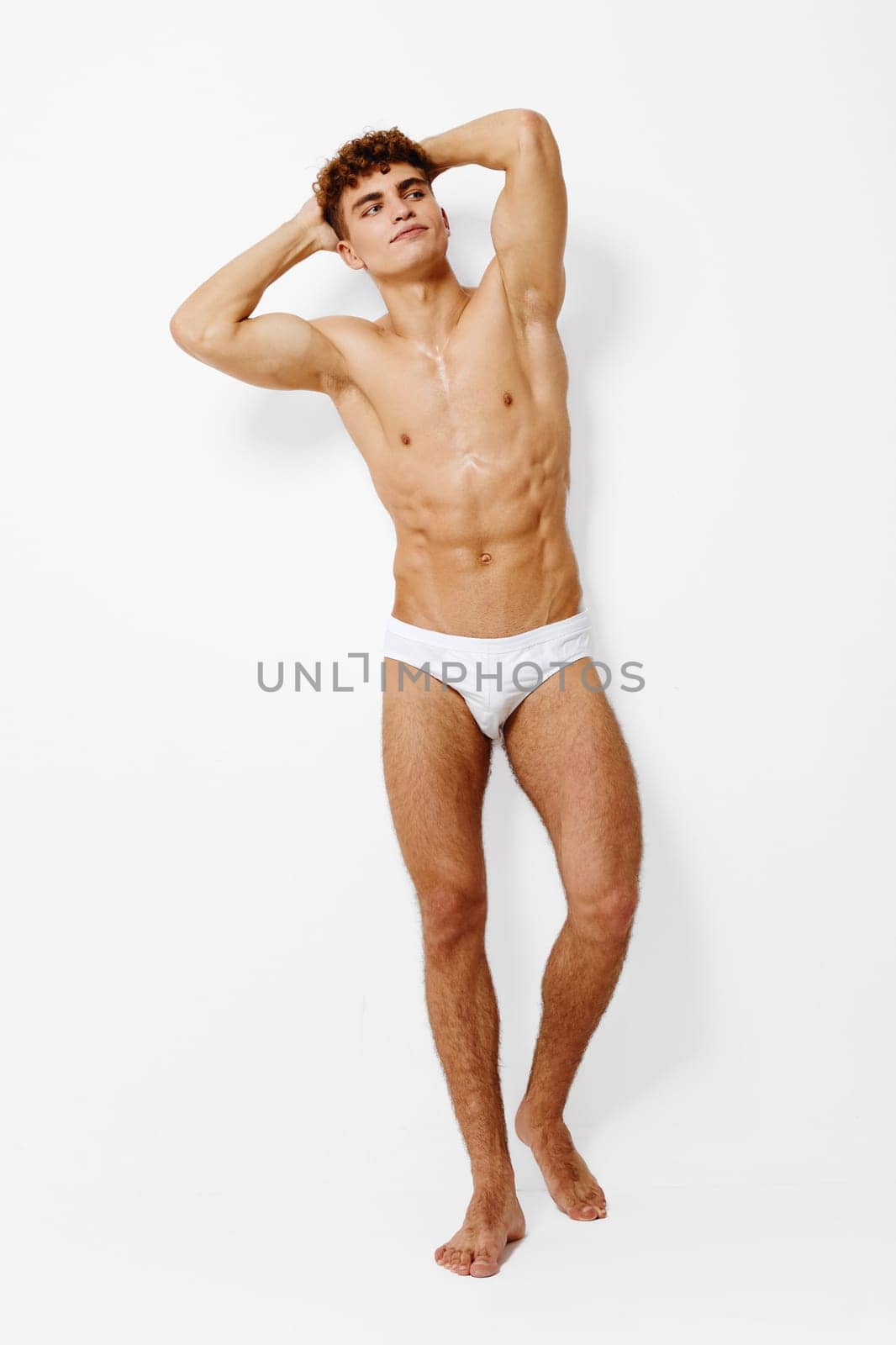 Fit male model stands with hands behind his head, highlighting toned body and strong posture. Minimalist style with a focus on confidence and body positivity.
