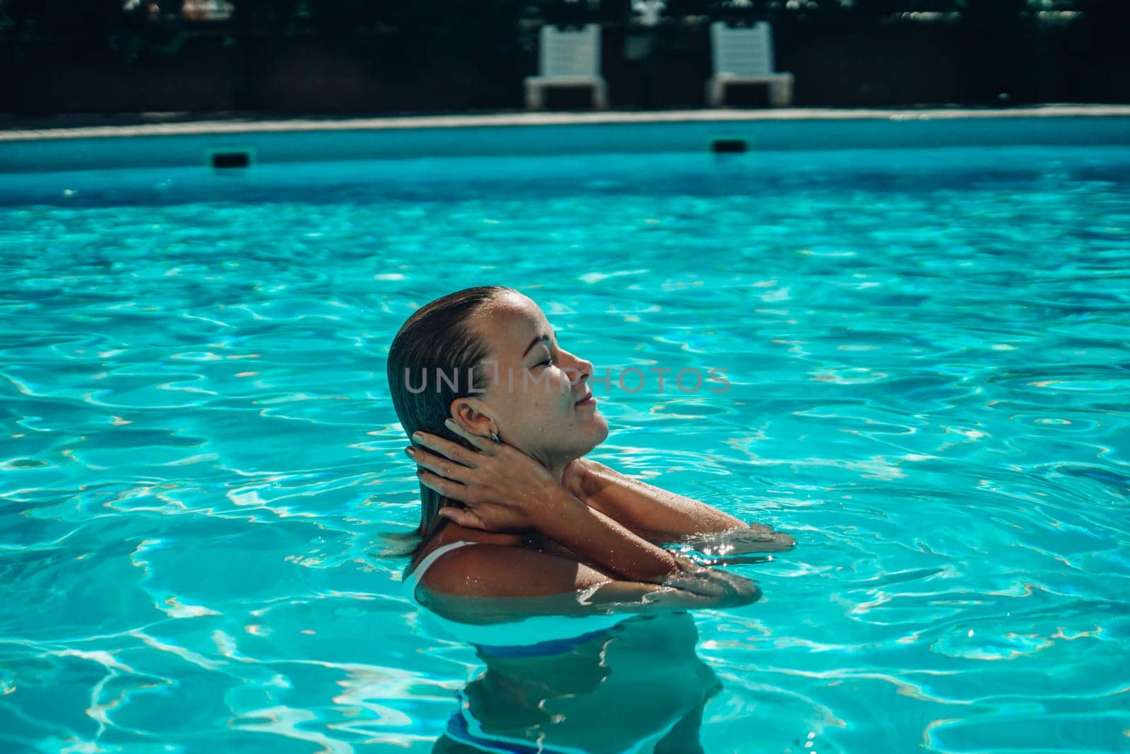 A woman is swimming in a pool. She is smiling and enjoying the water