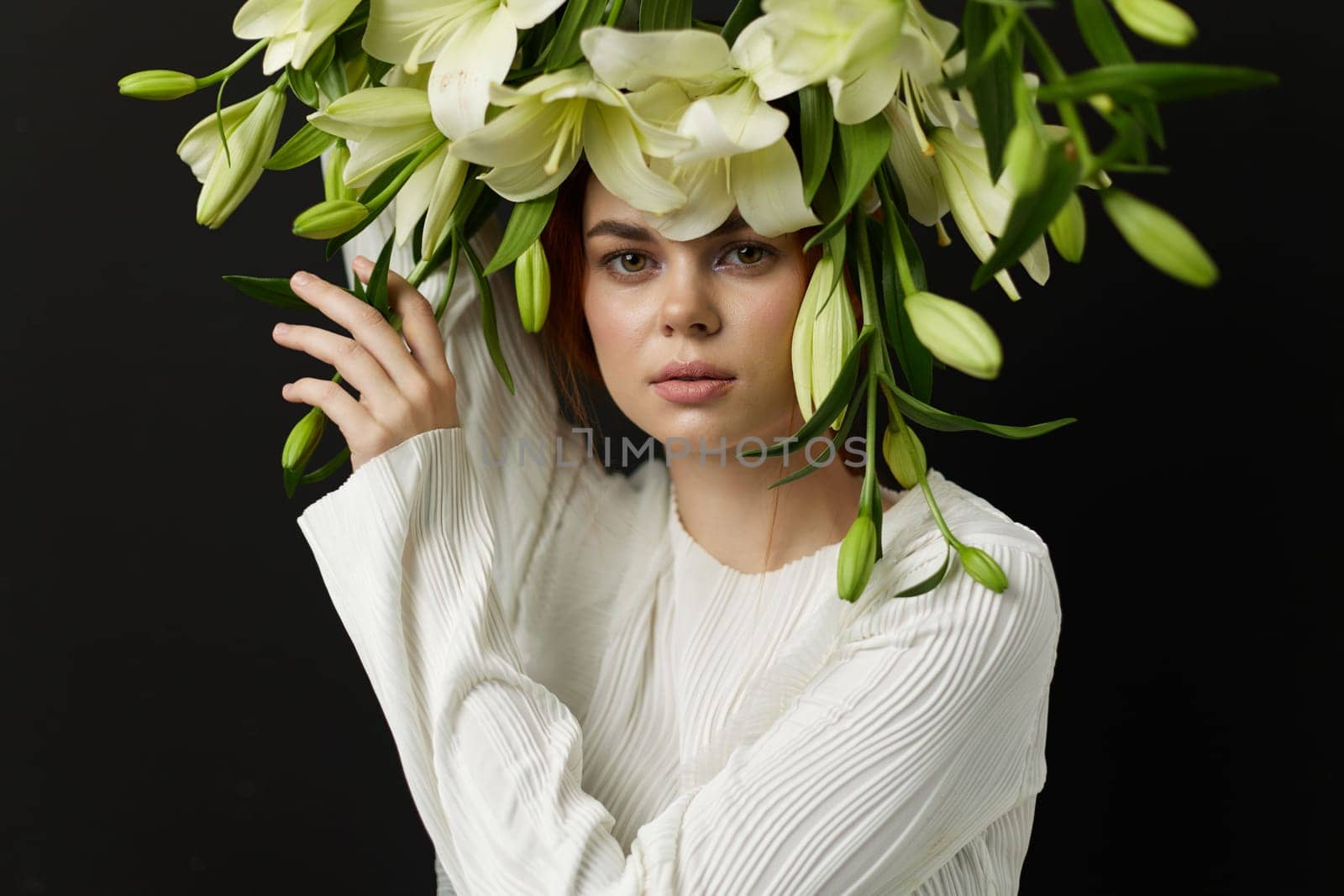 A young woman styled in a white outfit showcases a crown of flowers, embodying tranquility and elegance against a dark background, emphasizing nature s beauty