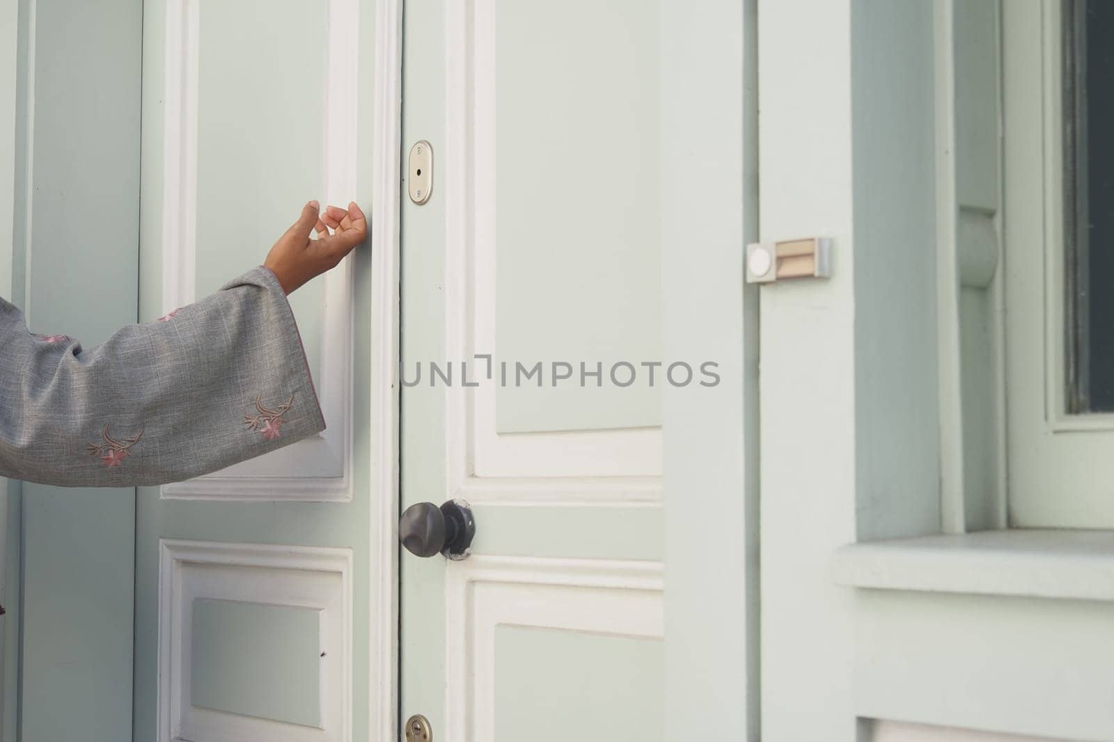 A hand is knocking lightly on a pastel green door while waiting.
