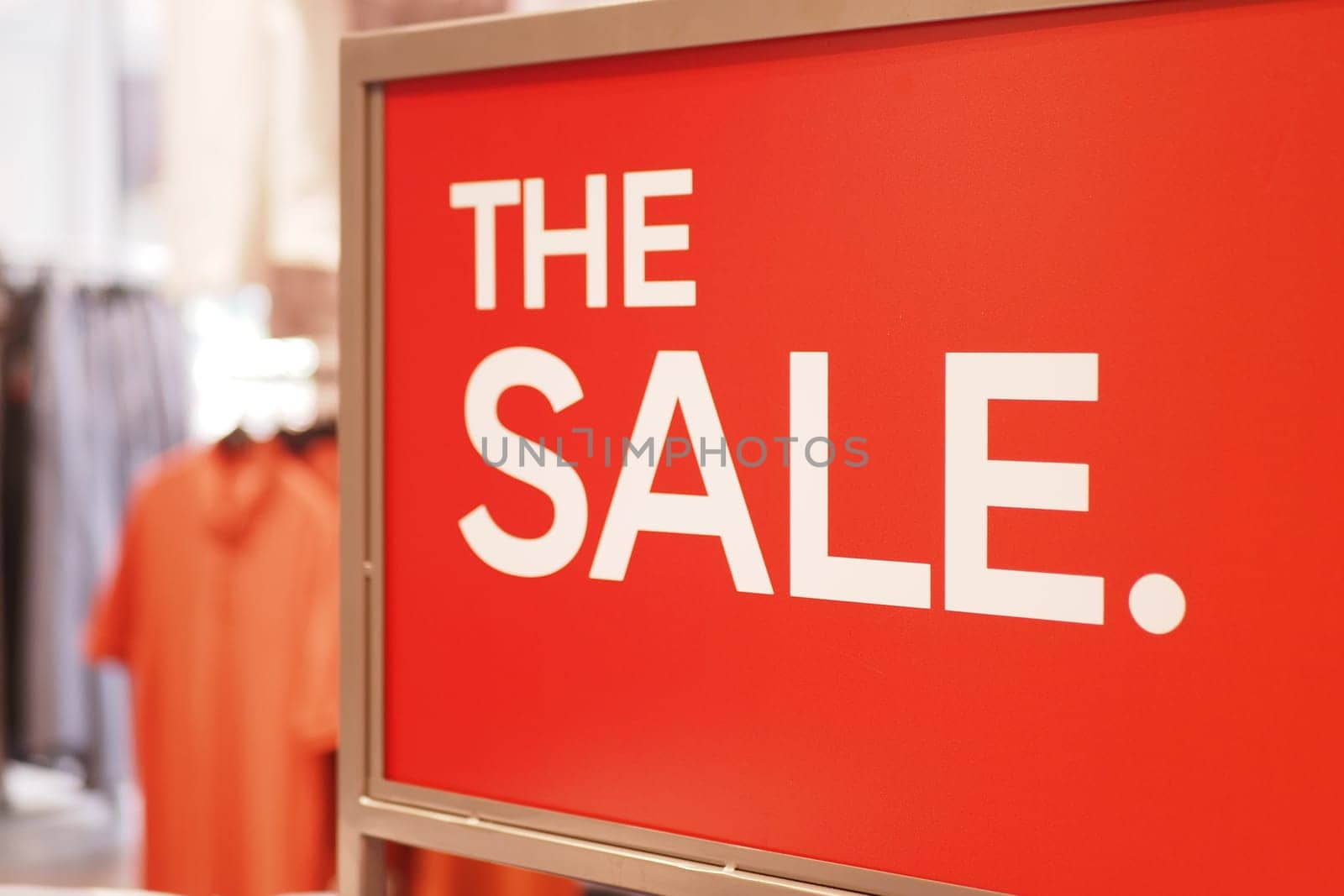 Bright red sign announces a sale at a retail location with clothing items.