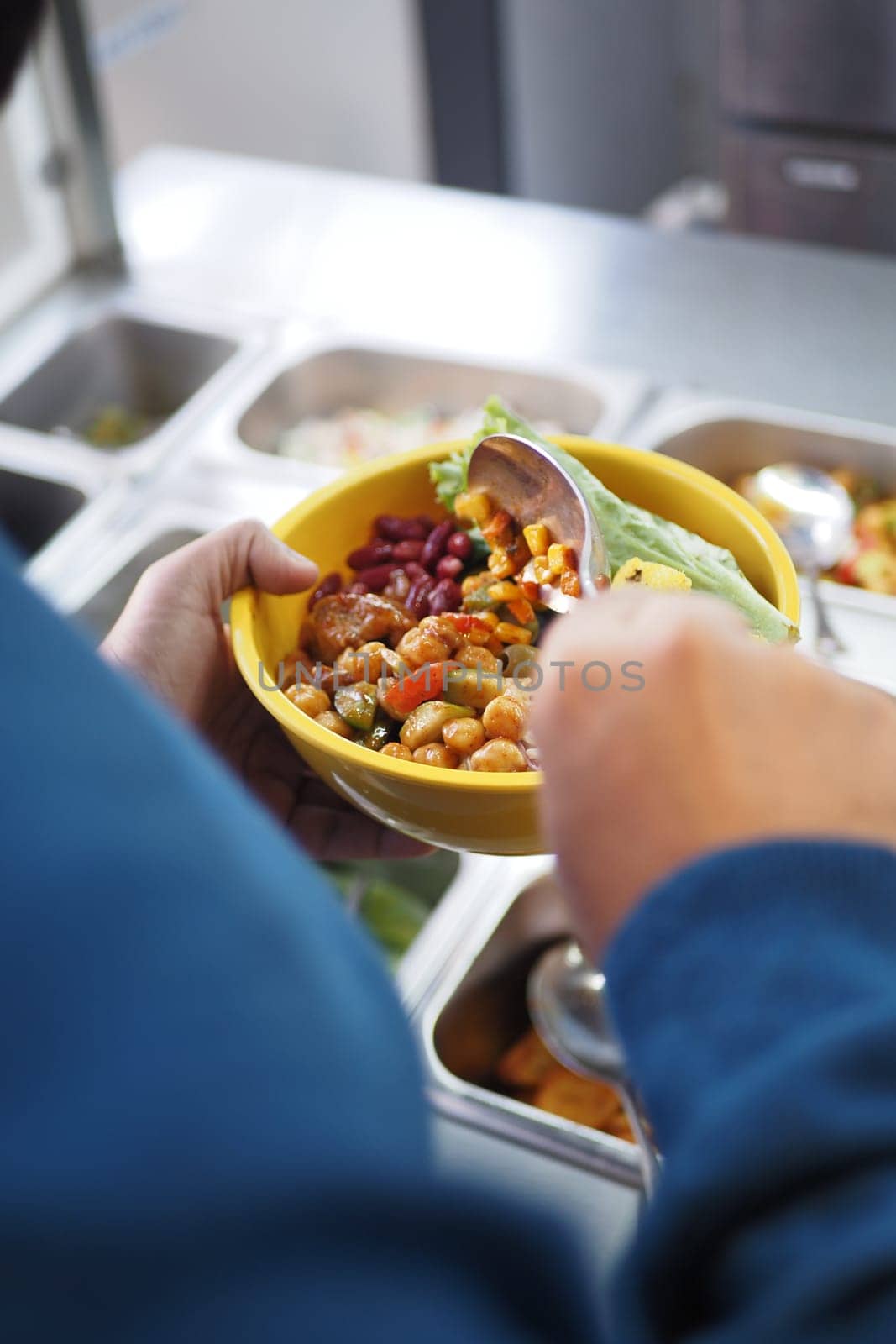 A person holds a yellow bowl filled with fresh vegetables and beans.