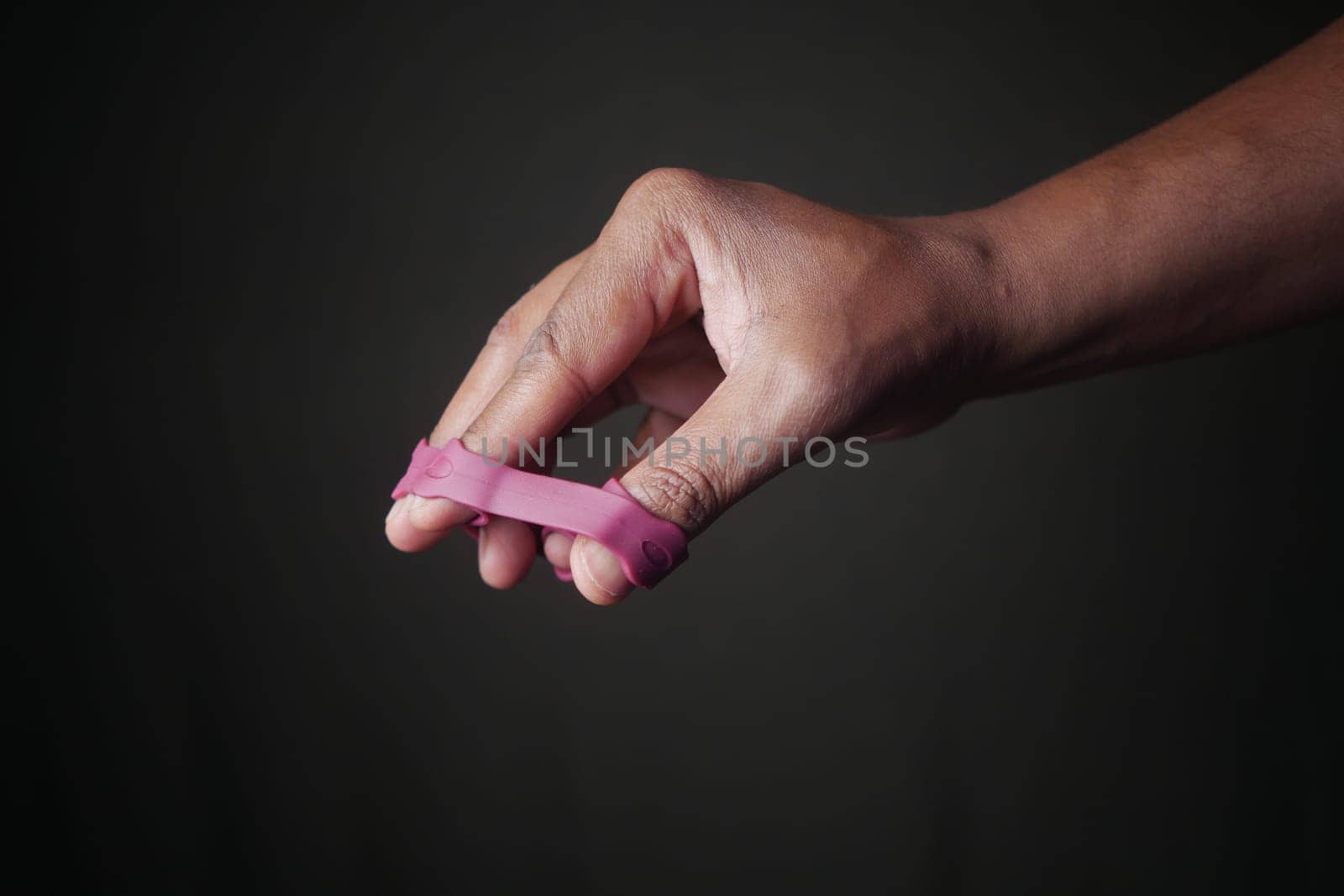 Close-Up of Hand with Pink Finger Exercise Tool Against Dark Background.