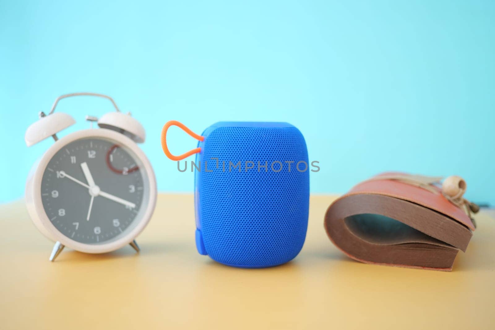 A blue portable speaker is placed between a clock and a shoe.