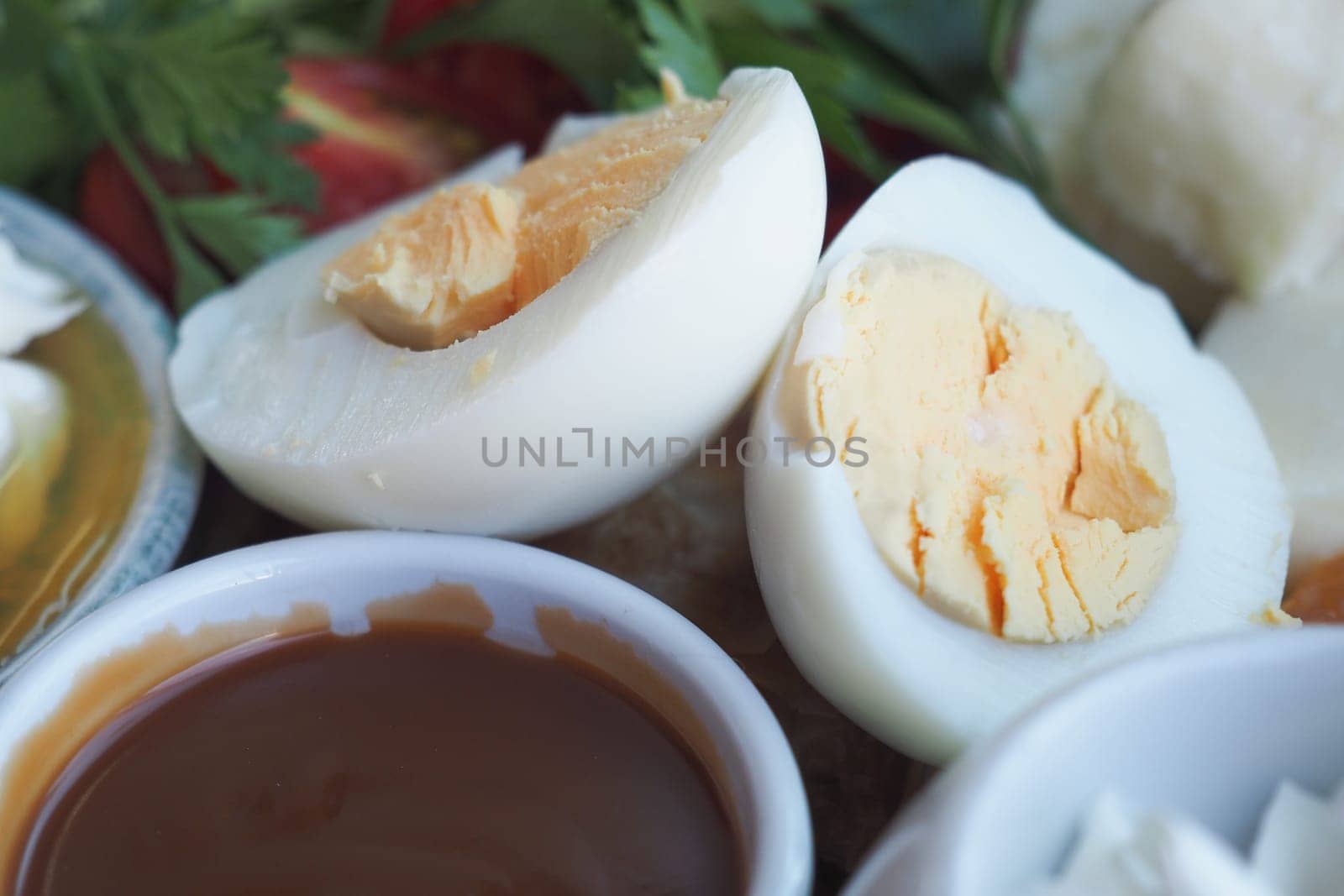 Boiled eggs cut in half alongside a savory dipping sauce and fresh herbs.