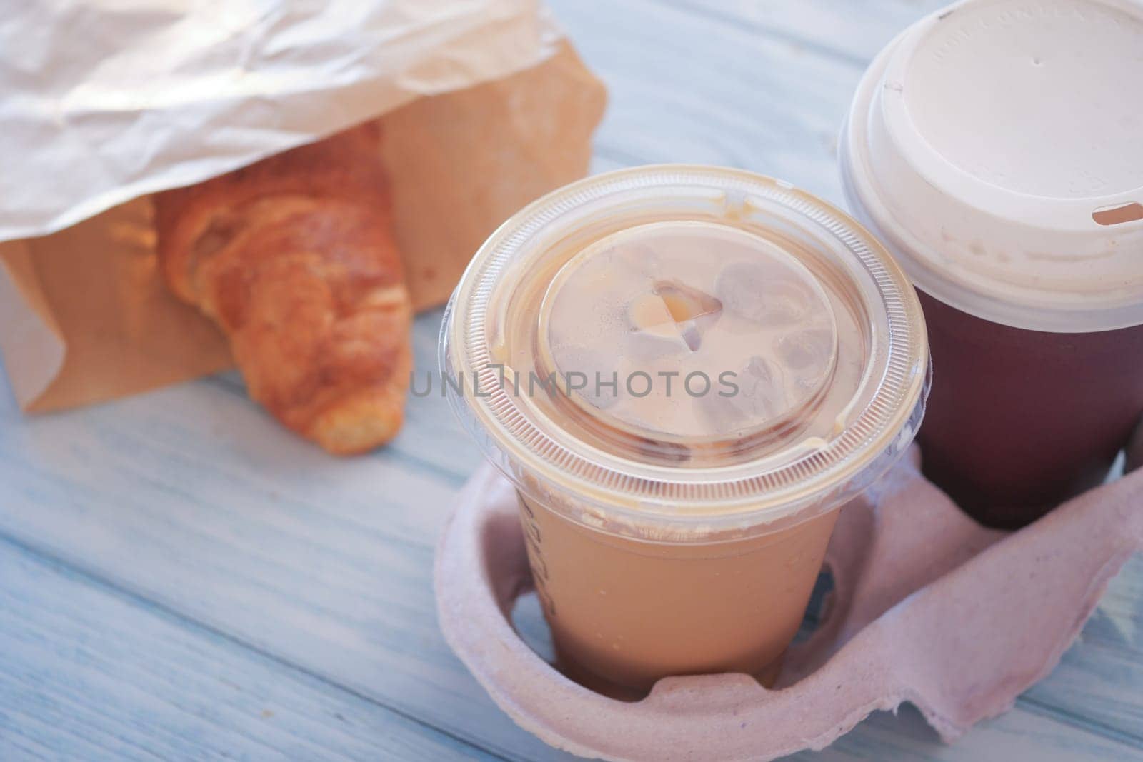 Iced coffee and a warm croissant are placed on a blue wooden table.
