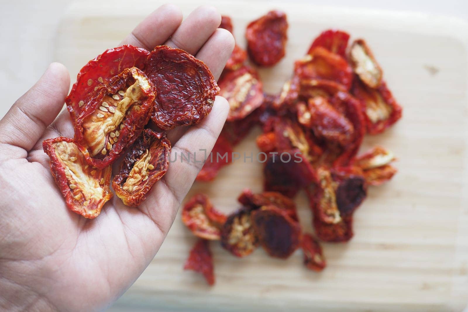 A hand holds dried tomatoes with more pieces scattered on a board.