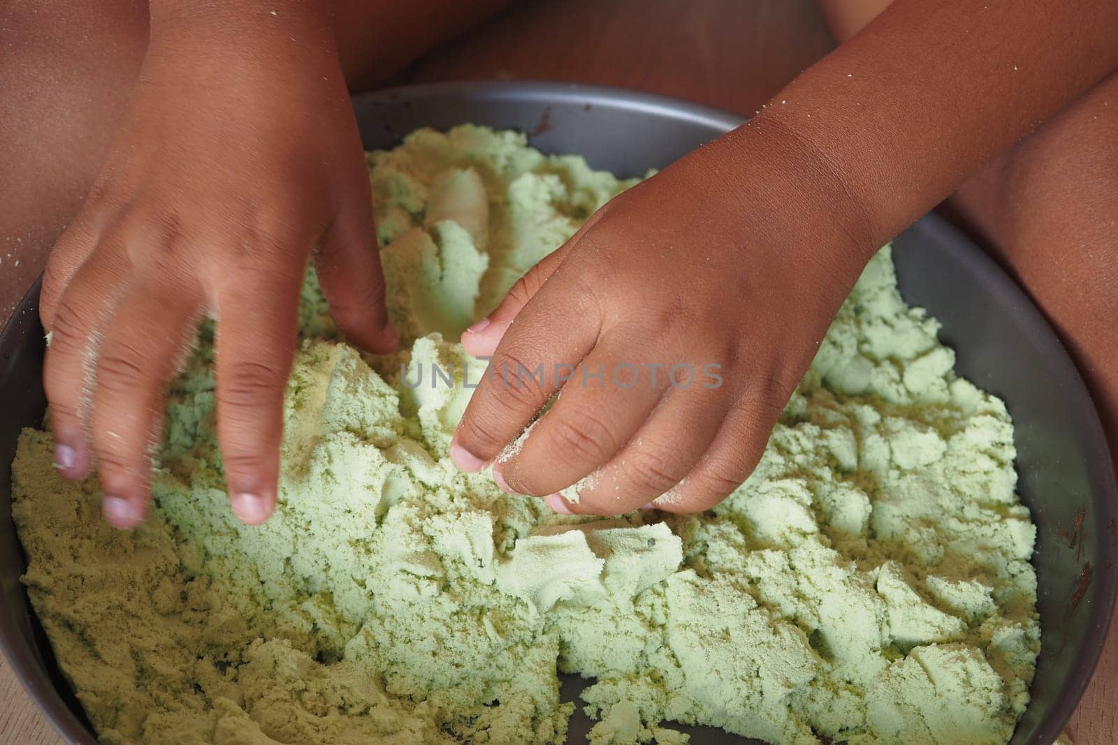 A child explores textured green sand with their hands in a tray.