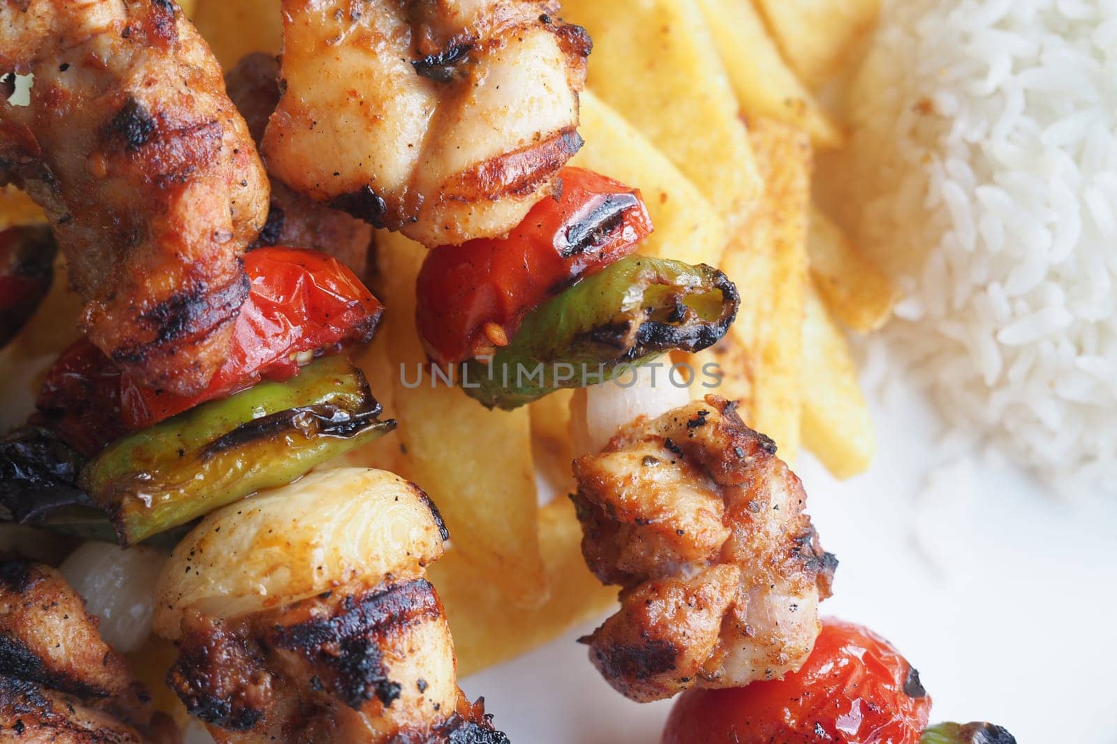 Juicy grilled chicken skewers with vegetables alongside rice and fries.