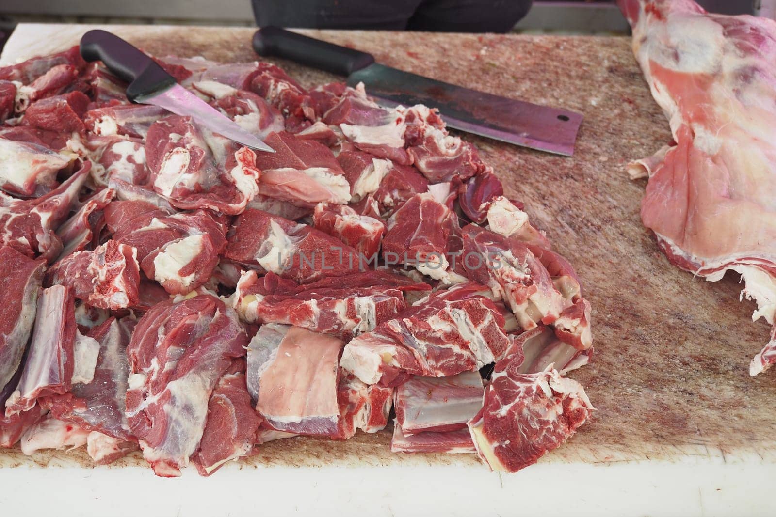 Butcher is cutting various meat pieces on a wooden block.