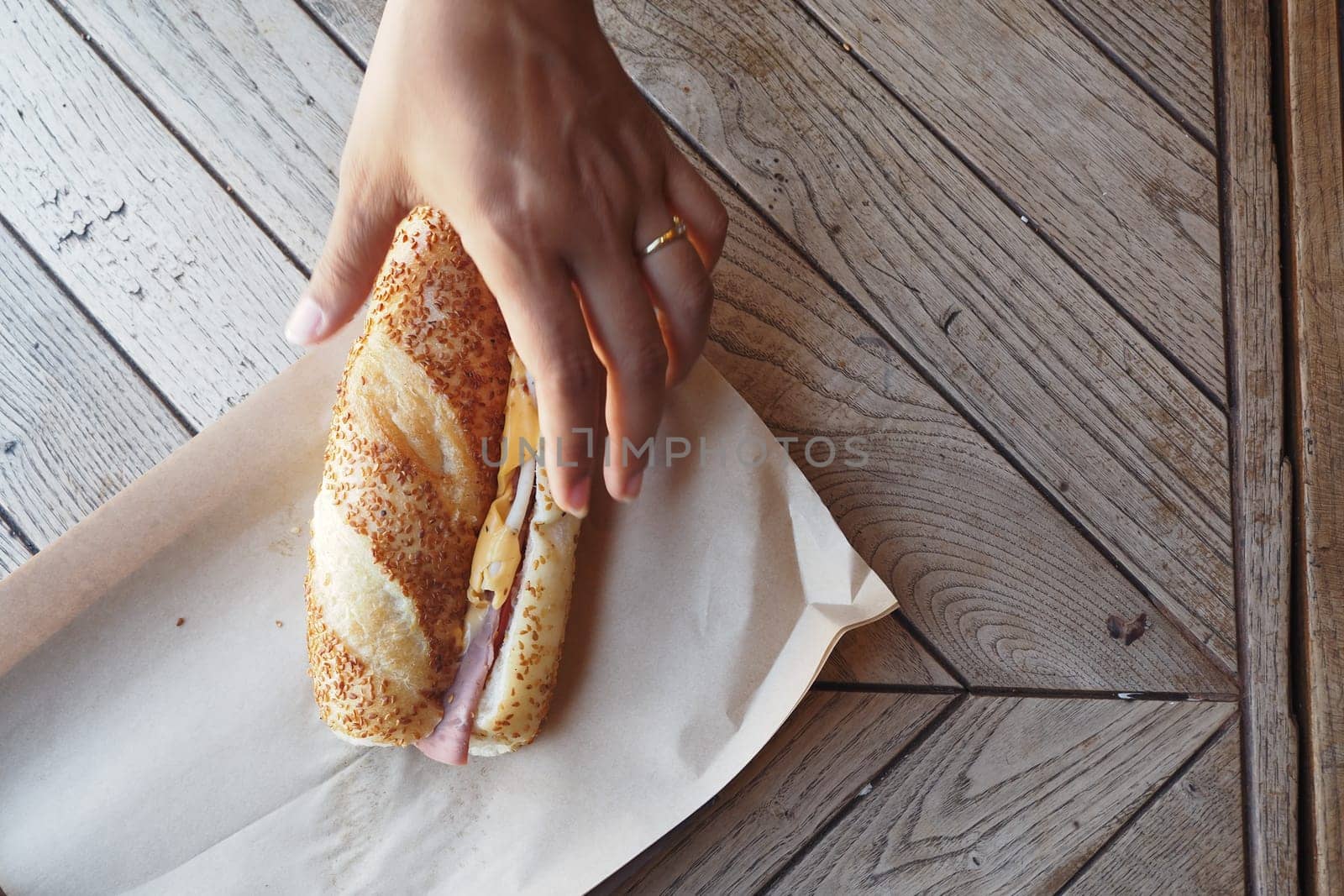 A hand is about to grab a sandwich placed on parchment paper.