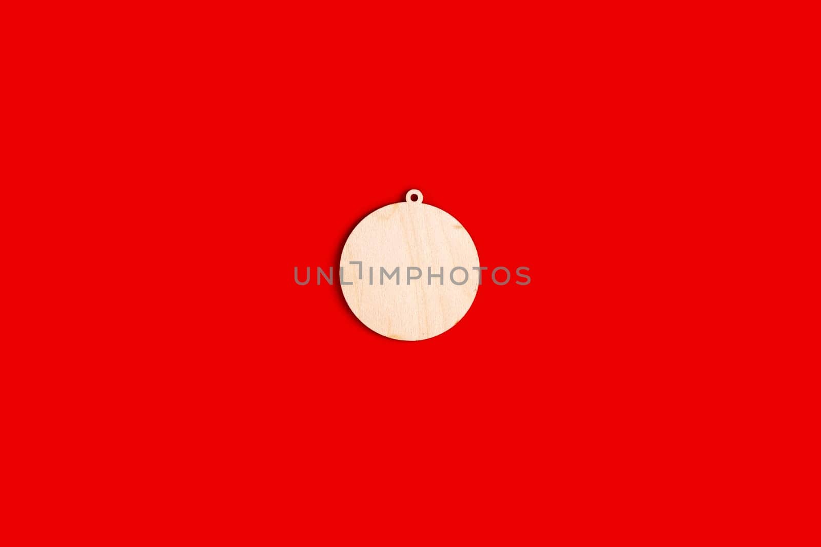 Wooden, flat, natural, unpainted shape of a Christmas ball on a red background. Close up. Copy space. Mock up. Top view