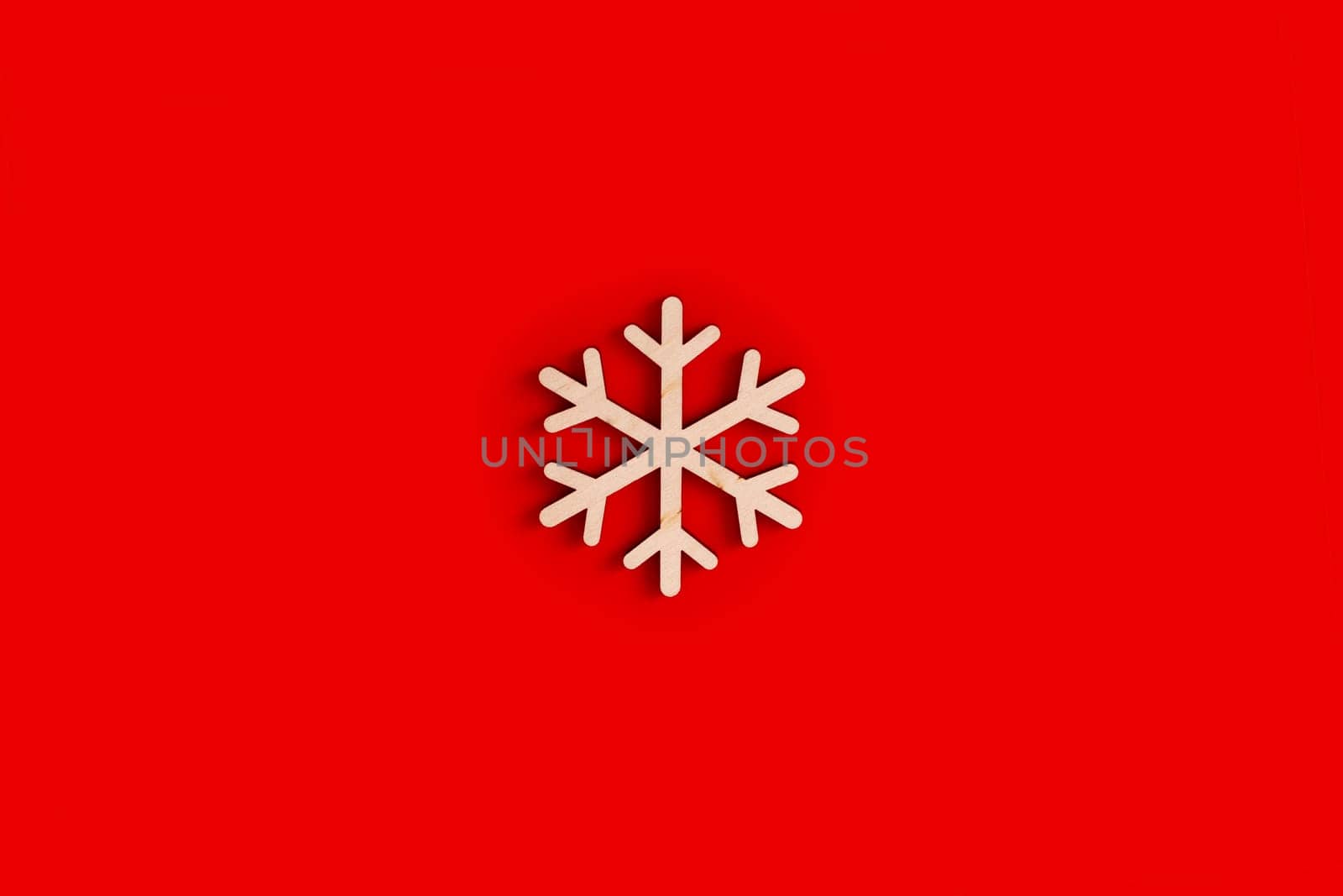 Flat natural unpainted wooden snowflake shape on red background. Close up. Copy space
