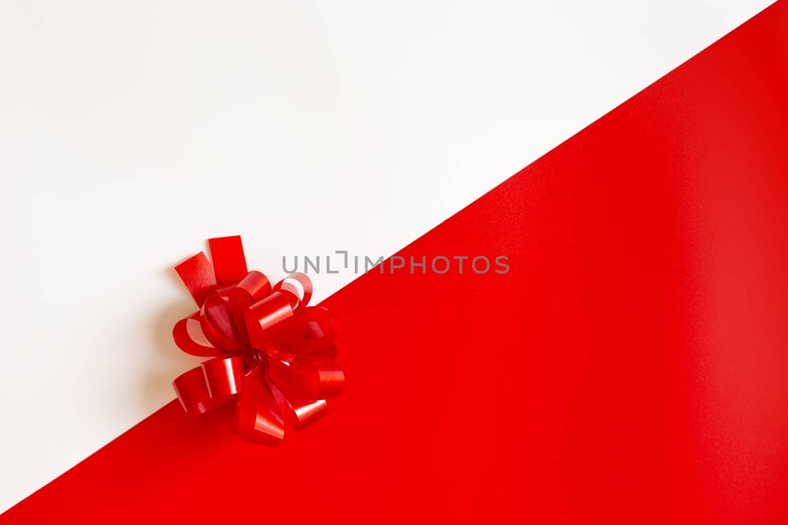 Red plastic bow on a red and white diagonal paper texture, lies in the middle, background for a template, horizontal. View from above. Mock up