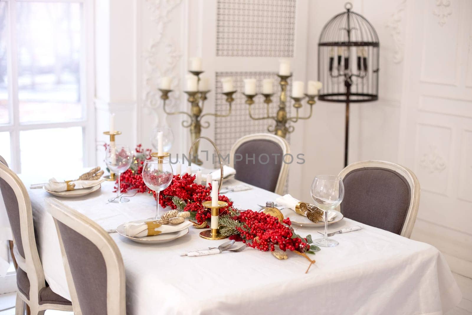 Festive Christmas and New Year table setting in natural and white colors with a red New Year garland and gold accessories, candles