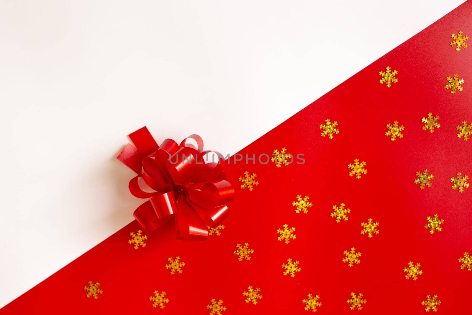 Red plastic bow on a red and white diagonal paper texture with golden snowflakes, lies in the middle, background for a template, horizontal. View from above. Mock up