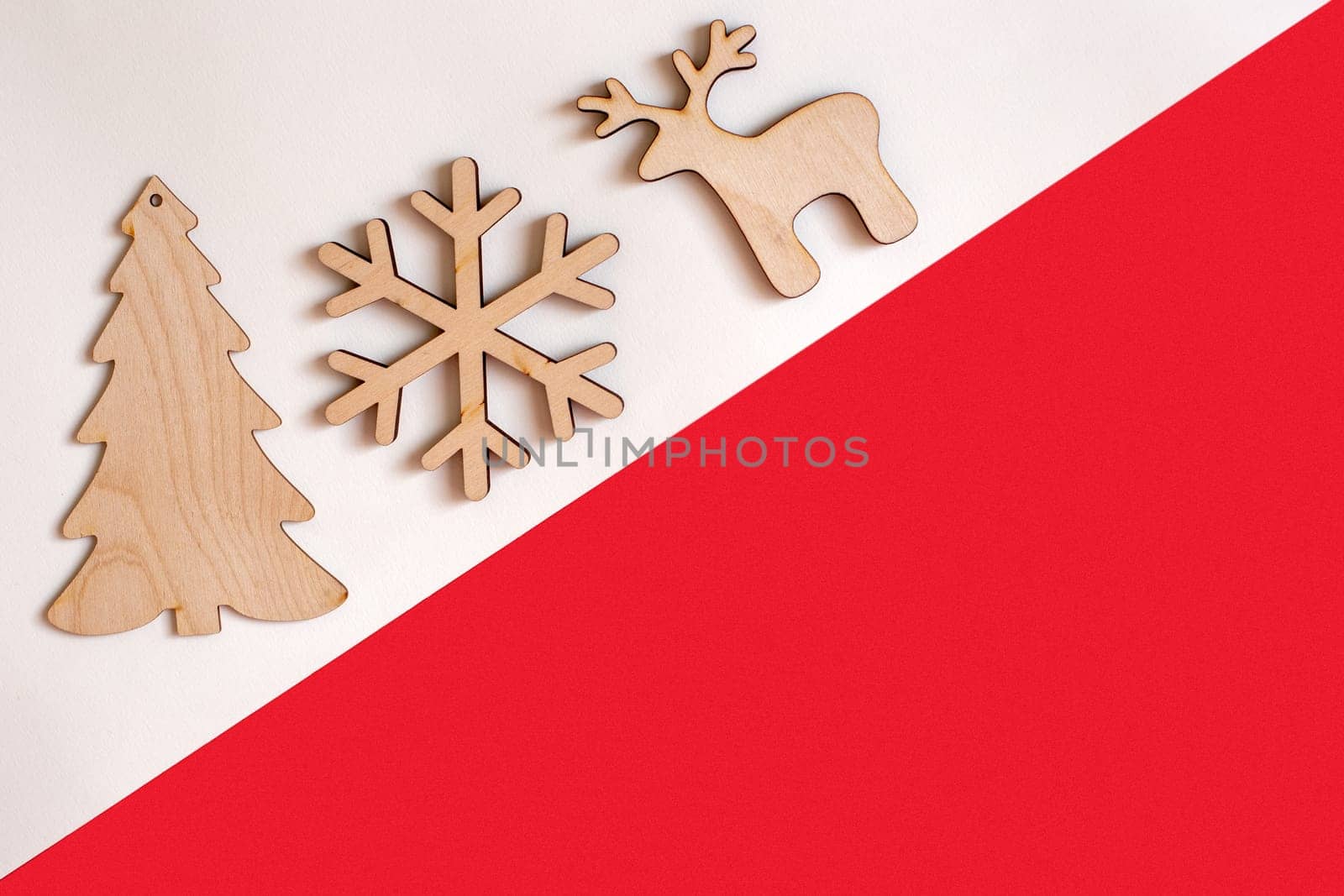 Flat natural unpainted wooden christmas decorations on white and red diagonal background: spruce, snowflake, deer. Copy space. Mock up
