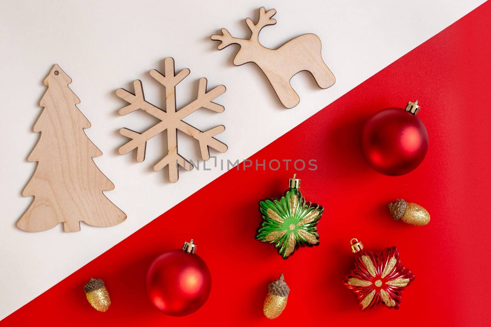 On a diagonal red and white background, flat natural unpainted wooden Christmas tree toys against plastic multi-colored toys. Copy space.Top view