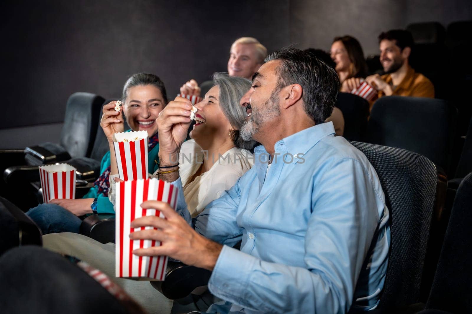 Groups of friends laughing and enjoying popcorn while watching an exciting movie in a cozy cinema auditorium, sharing moments of joy together