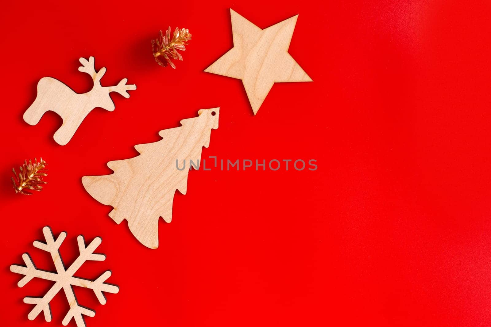 Flat natural unpainted wooden Christmas decorations: star, snowflake, deer and spruce and golden cones lie diagonally on red background. Copy space. Mock up