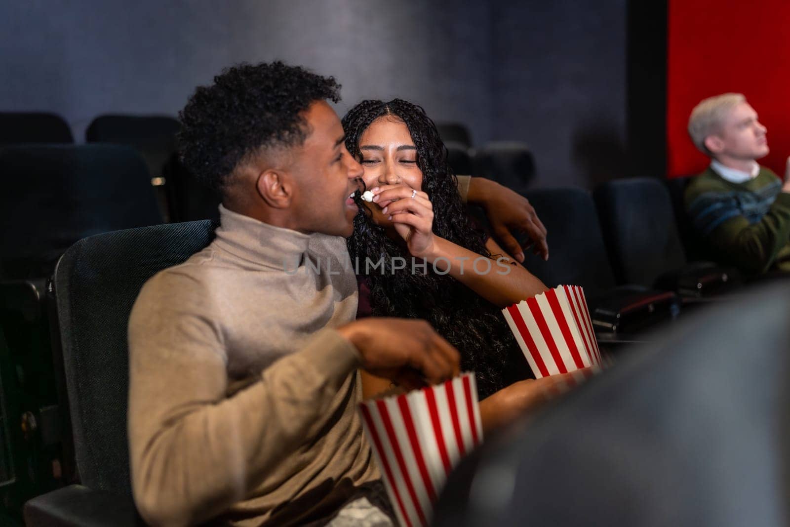 Young couple enjoys a movie date, sharing popcorn and affection while watching a film in a cinema