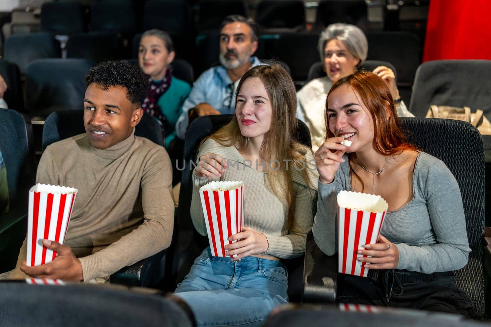 Group of friends watching a film at the movie theatre, eating popcorn and enjoying their leisure time